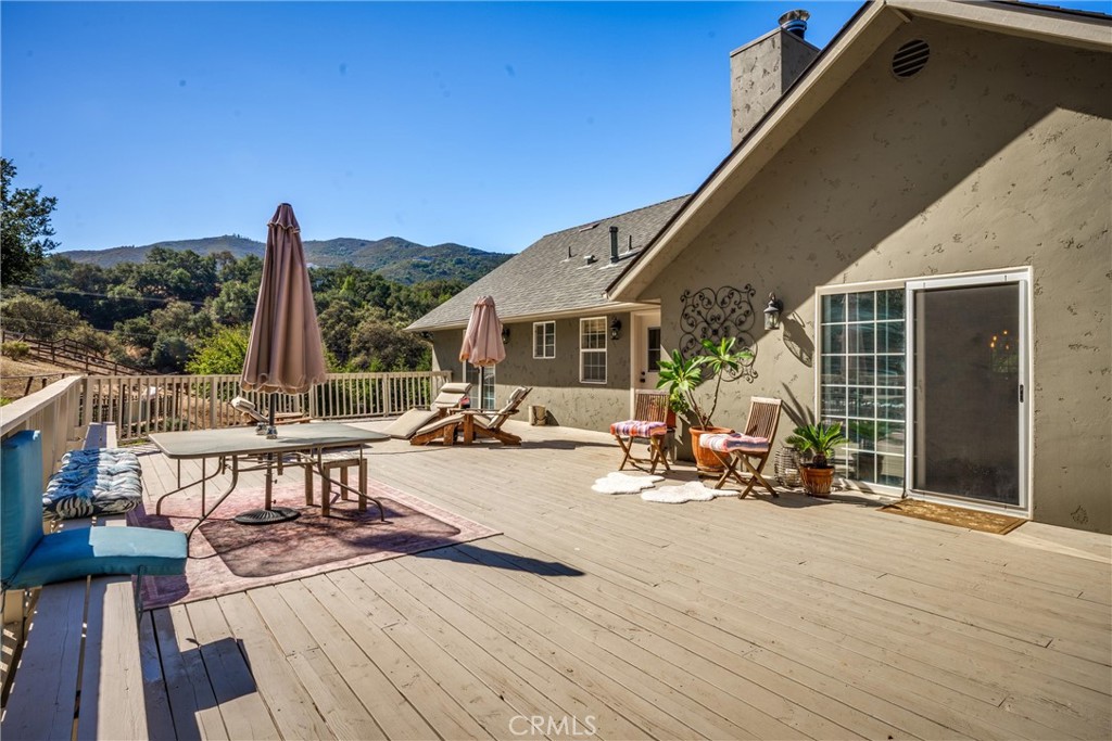 Spacious wooden deck with patio seating and umbrellas overlooking rolling green hills.