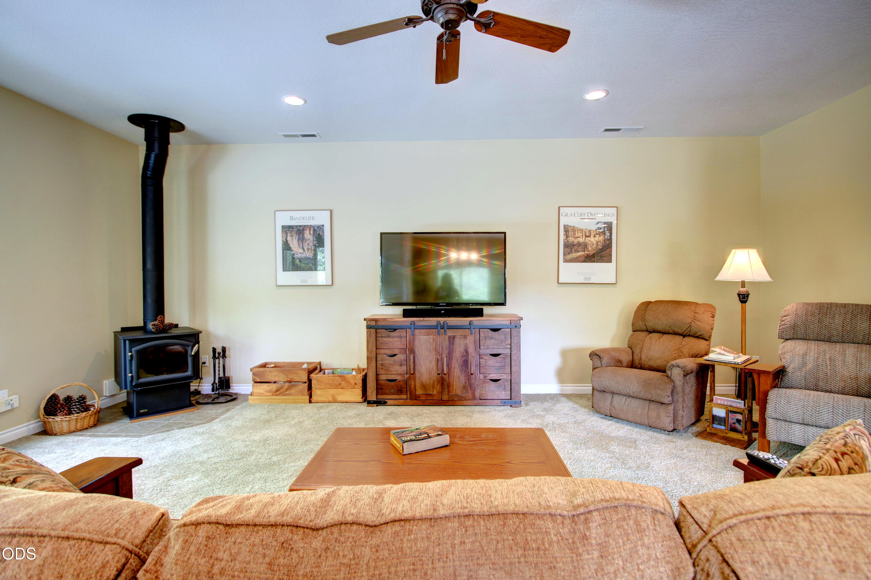 Living room with a wood-burning stove, wooden media console, ceiling fan, and recliners.