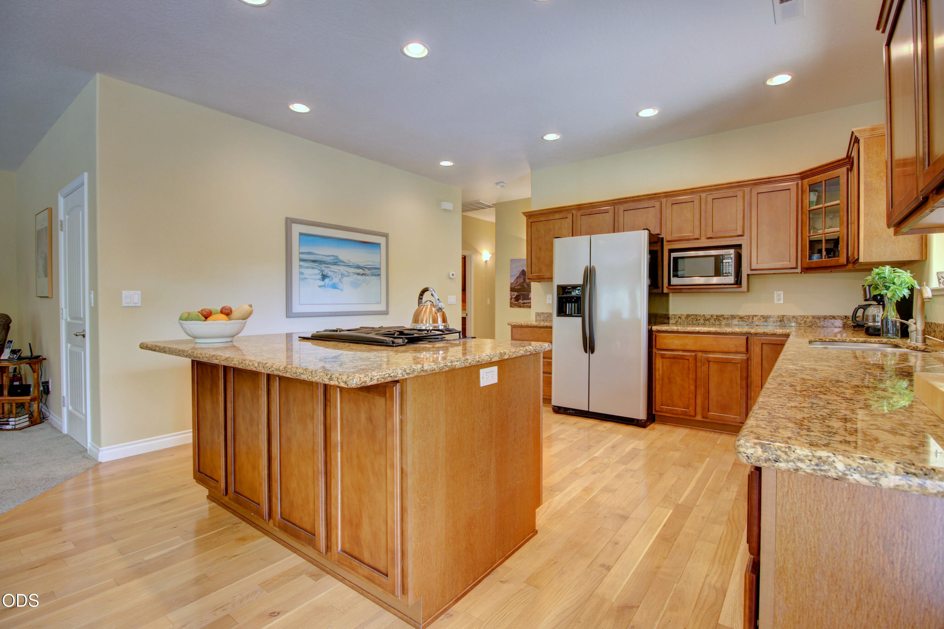 Kitchen with a large granite island, warm wood cabinetry, and stainless steel appliances.