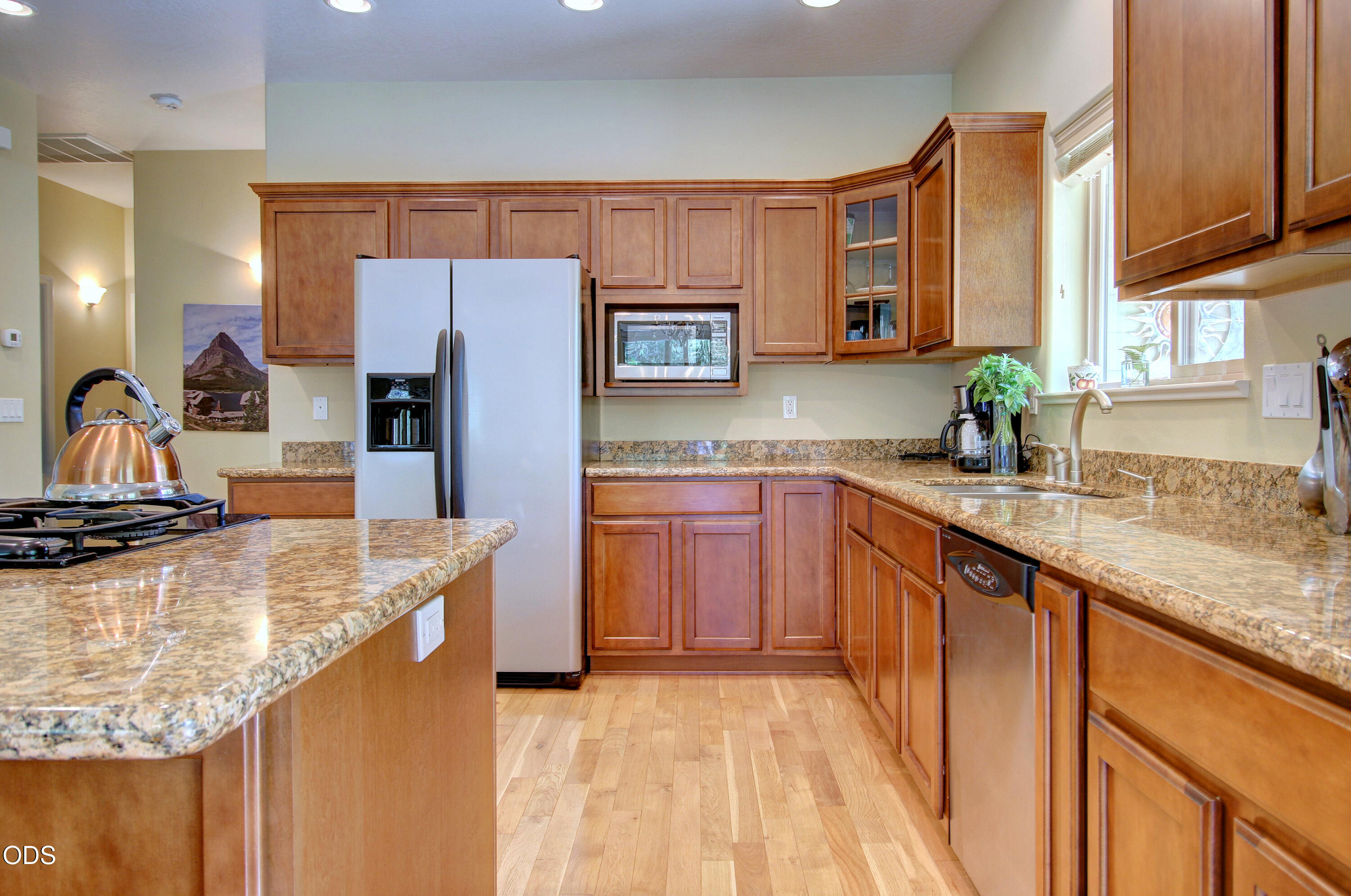 Kitchen with wood cabinetry, granite counters, a gas cooktop island, and a sink beneath a bright window.