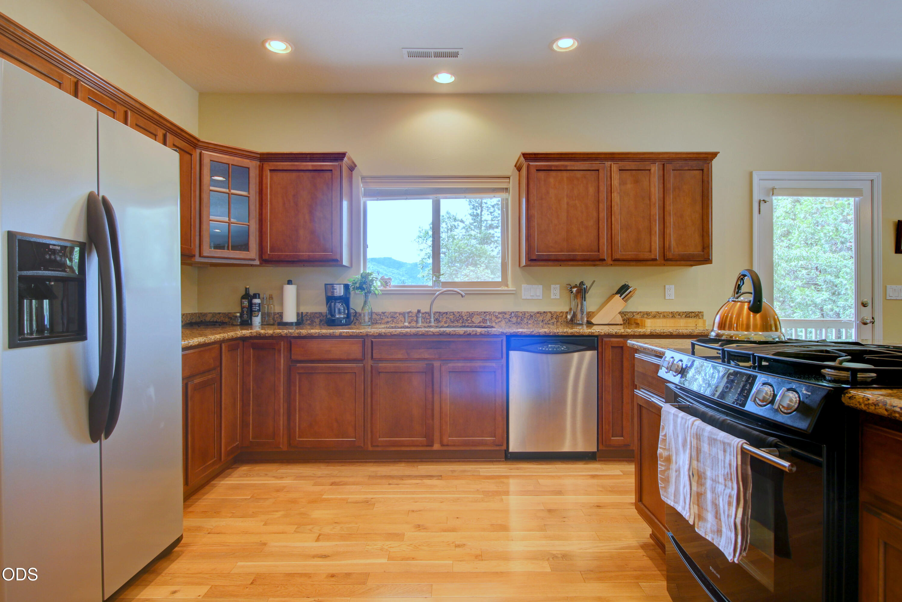 Kitchen with wood cabinetry, granite counters, hardwood floors, and a window overlooking trees and distant hills.