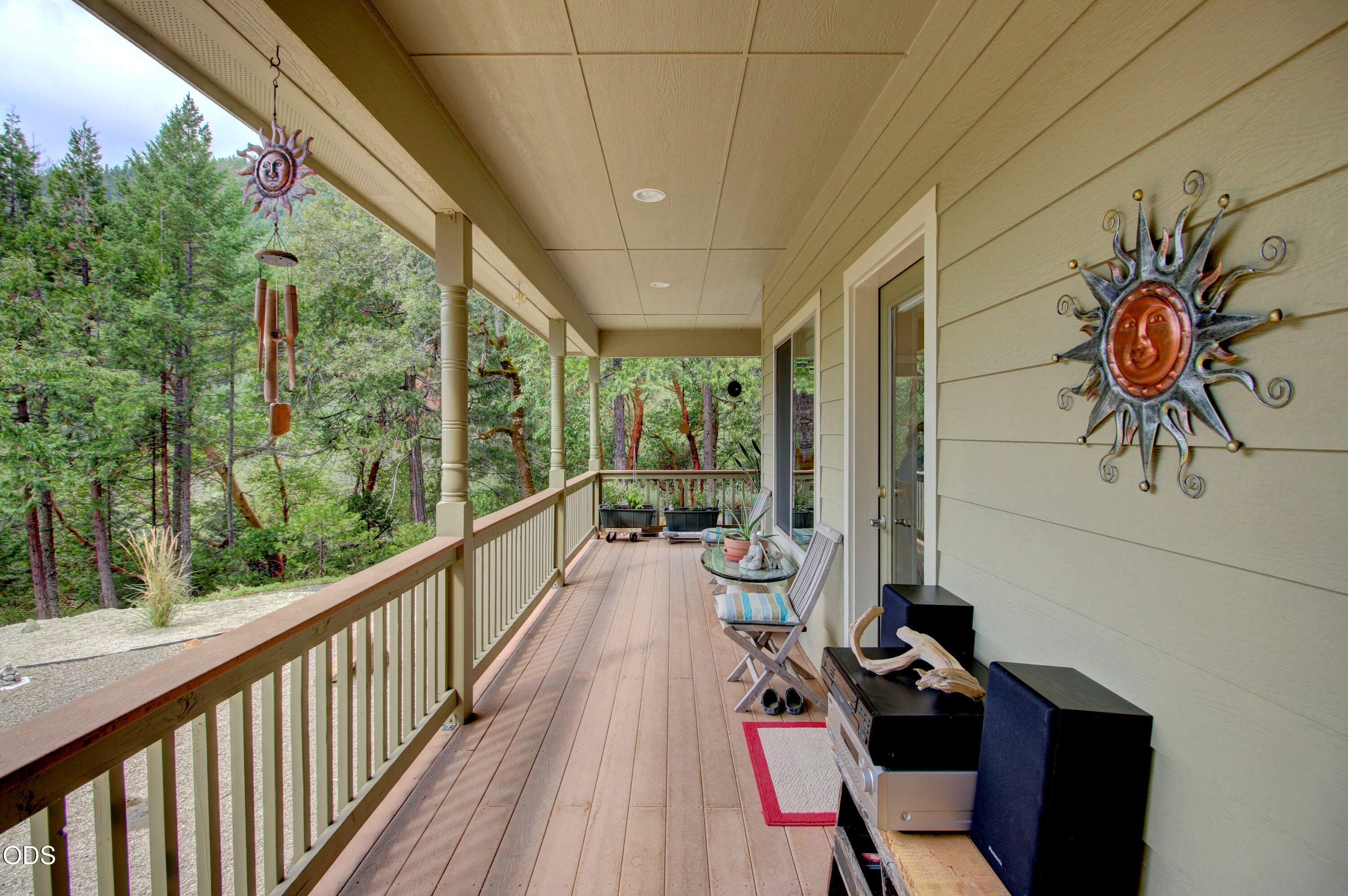 Covered porch with outdoor seating and sun decorations overlooking tall trees.
