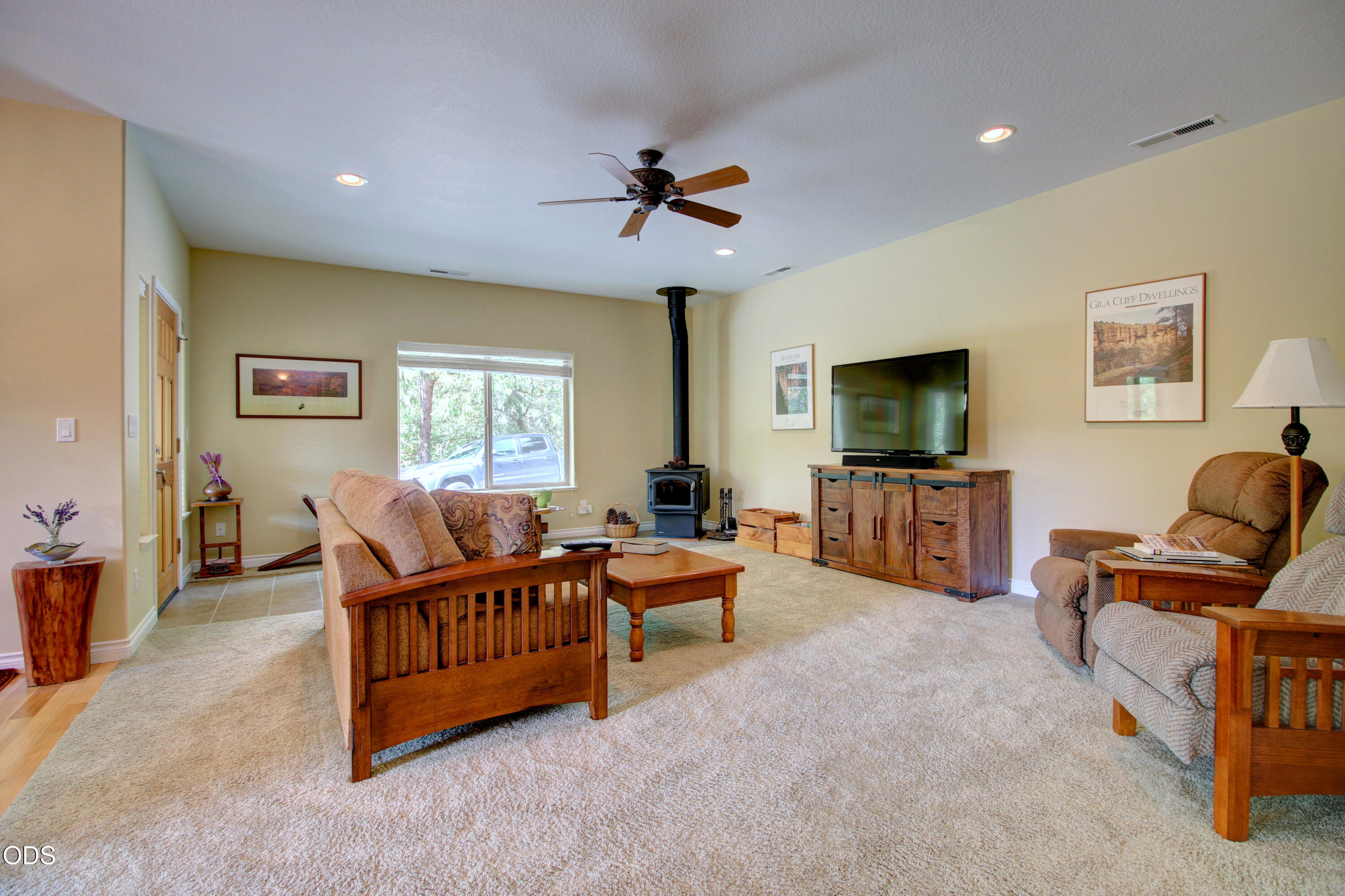 Furnished living room with a freestanding wood stove, wooden furniture, and a large window.