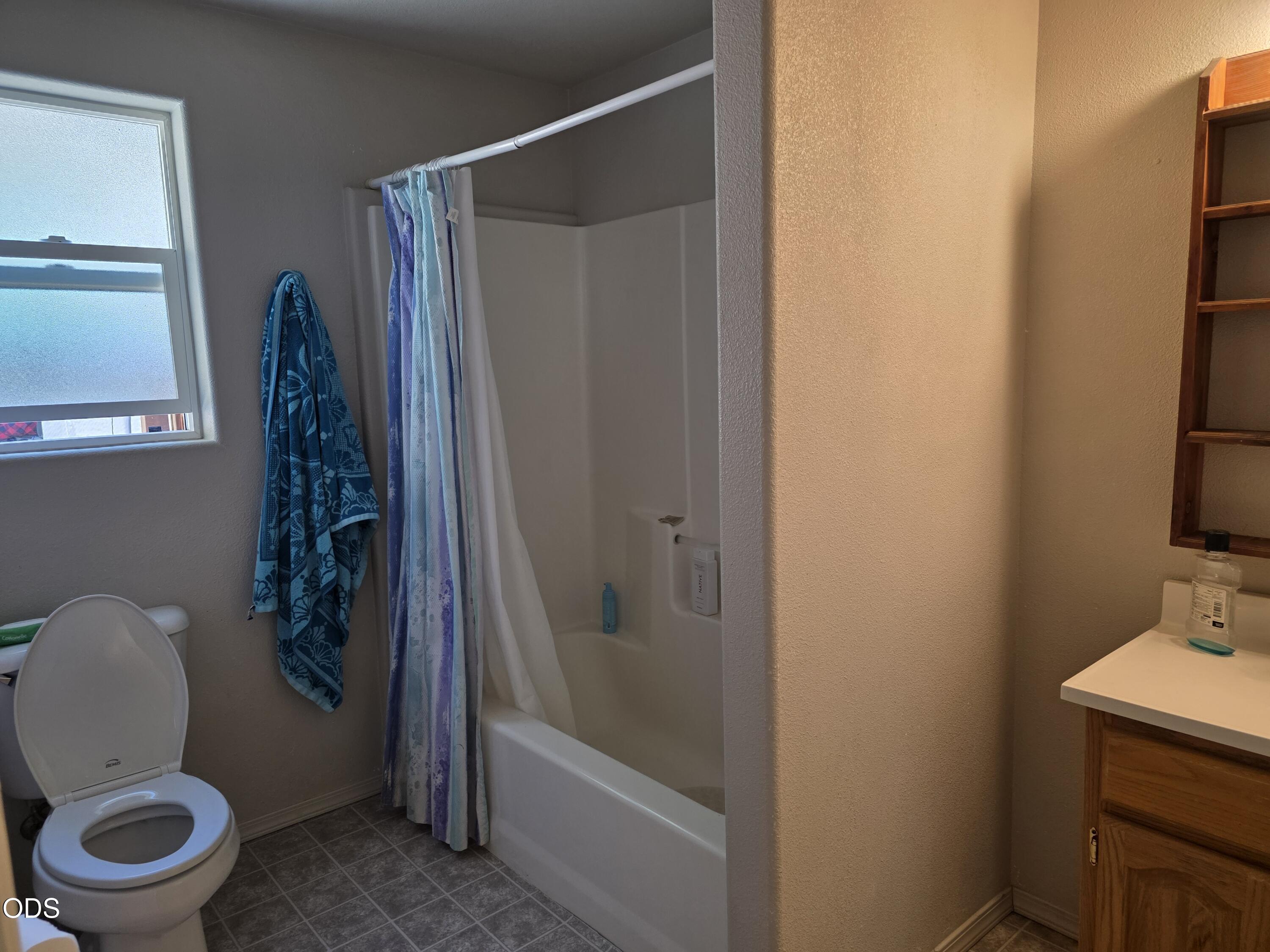 Bathroom with a toilet, bathtub and shower curtain, frosted window, and wood vanity.