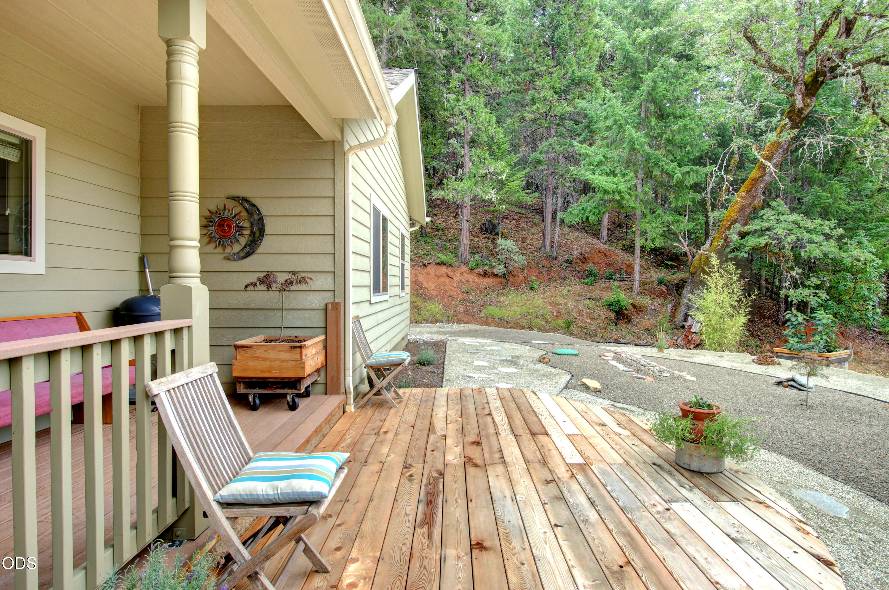 Wooden deck beside the house, furnished with chairs and overlooking a wooded hillside.