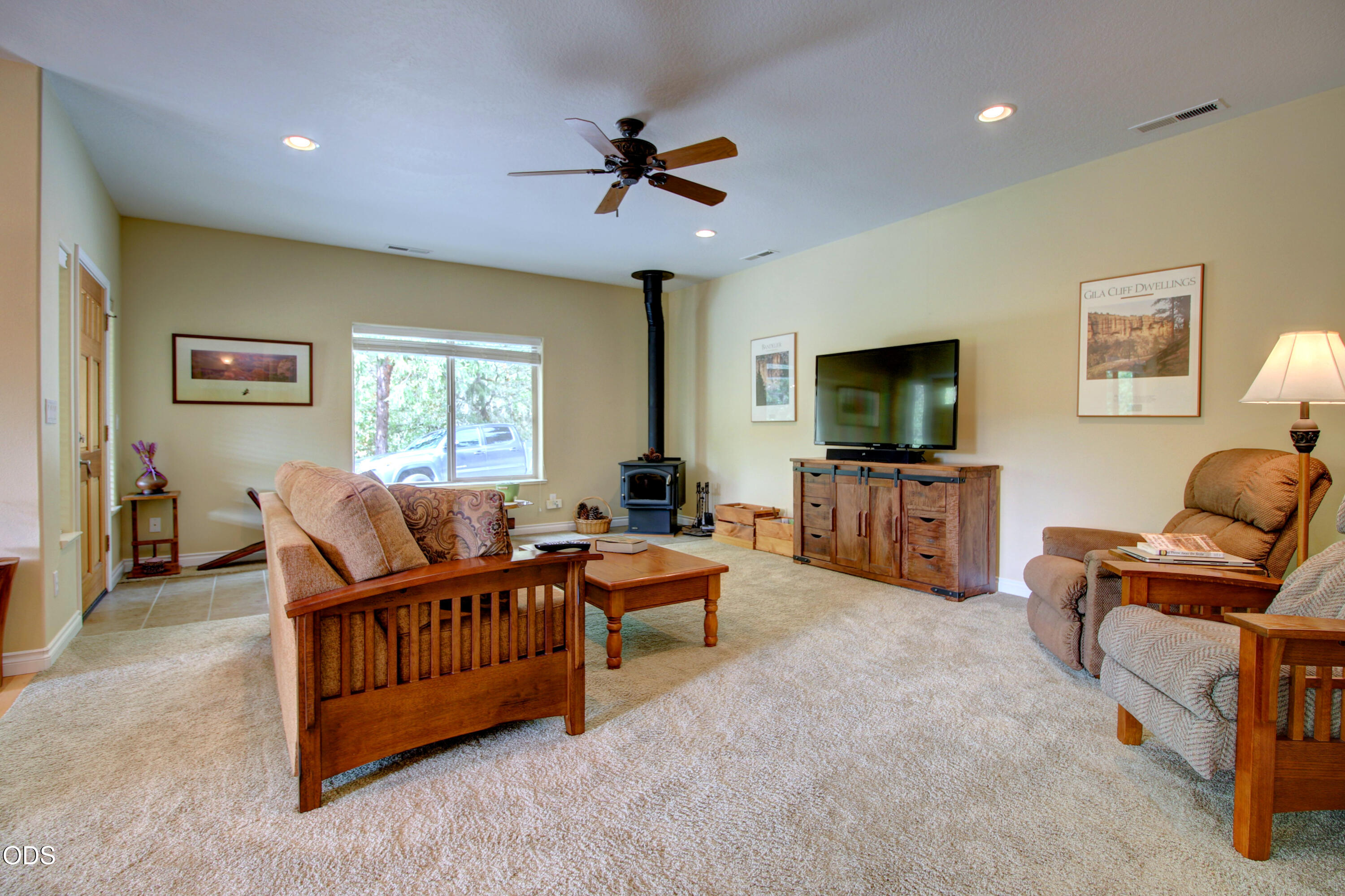 Furnished living room with a black wood stove, rustic TV cabinet, and large window.