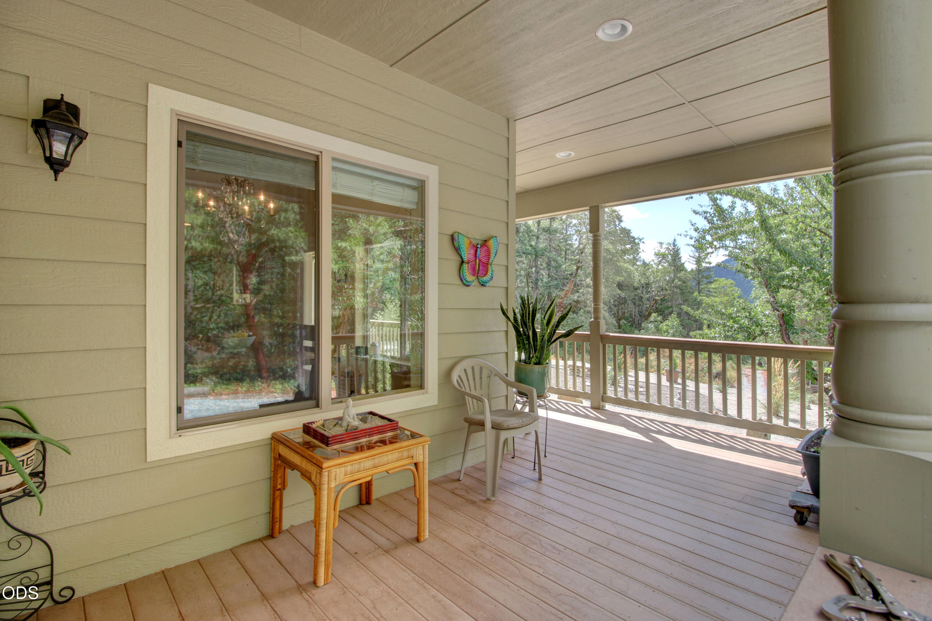 Covered porch with a wicker table and chair overlooking leafy trees and a distant mountain.