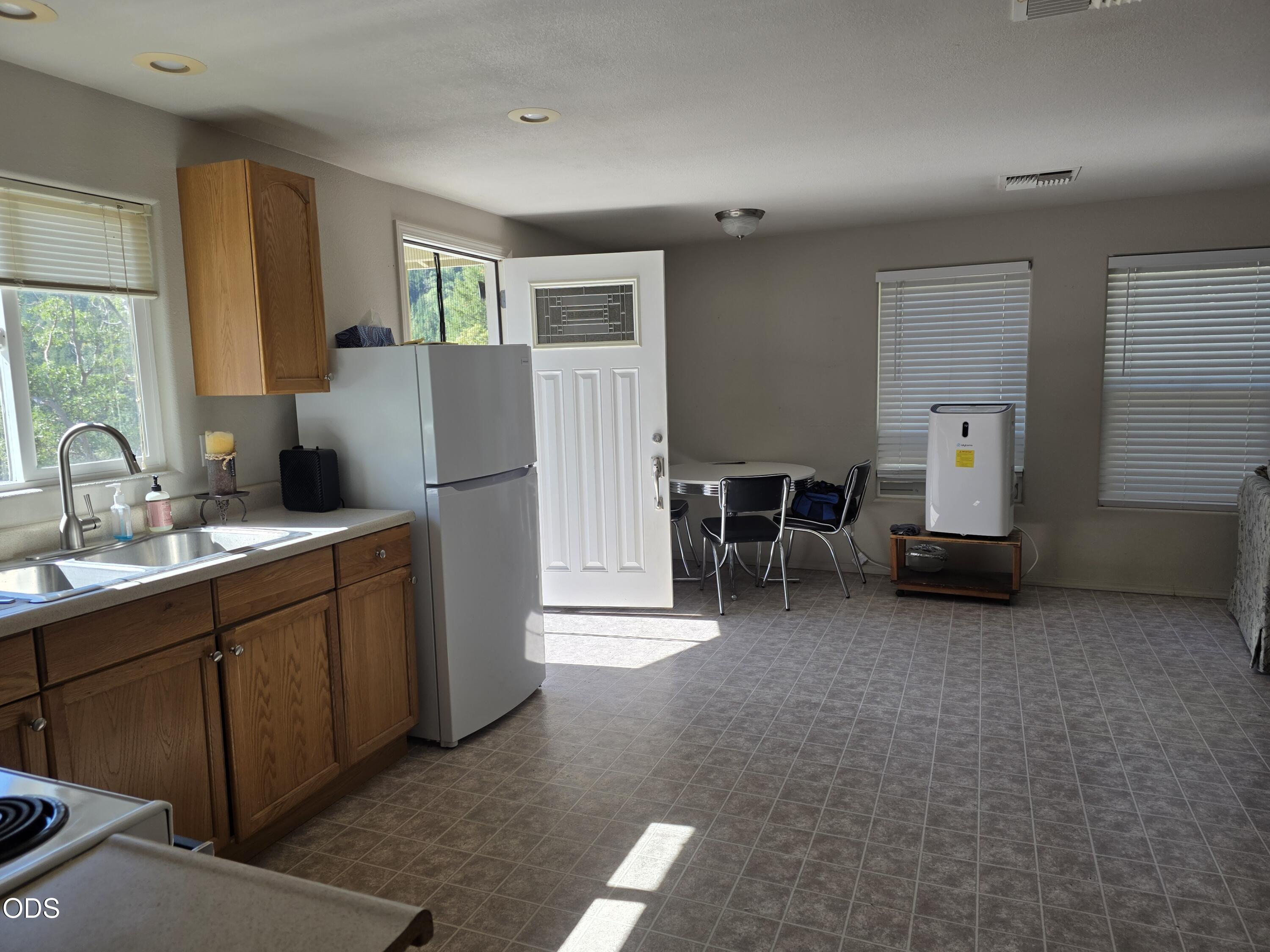 Kitchen and dining area with wood cabinets, a white refrigerator, and sunlight across the tiled floor.