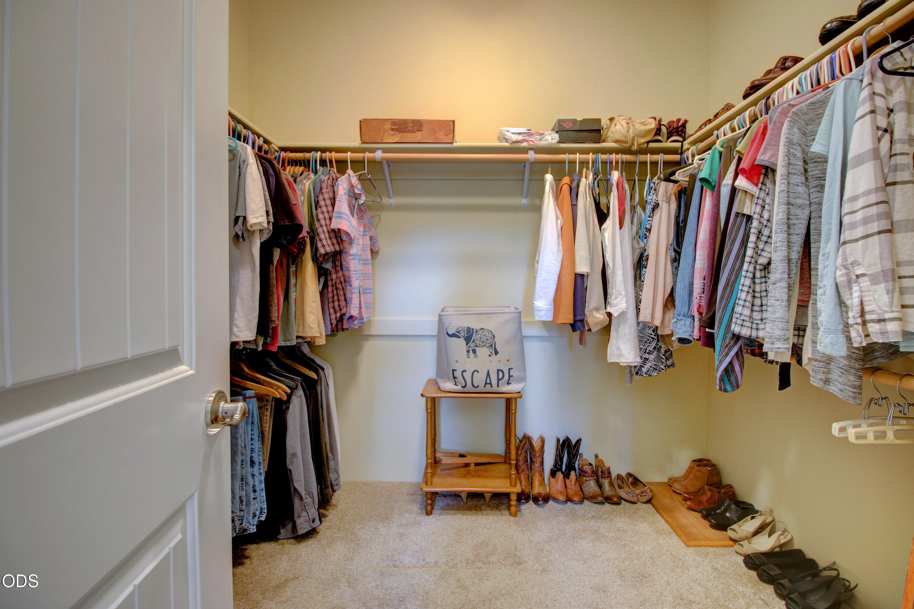 Walk-in closet with clothes on three sides and shoes arranged along the floor.