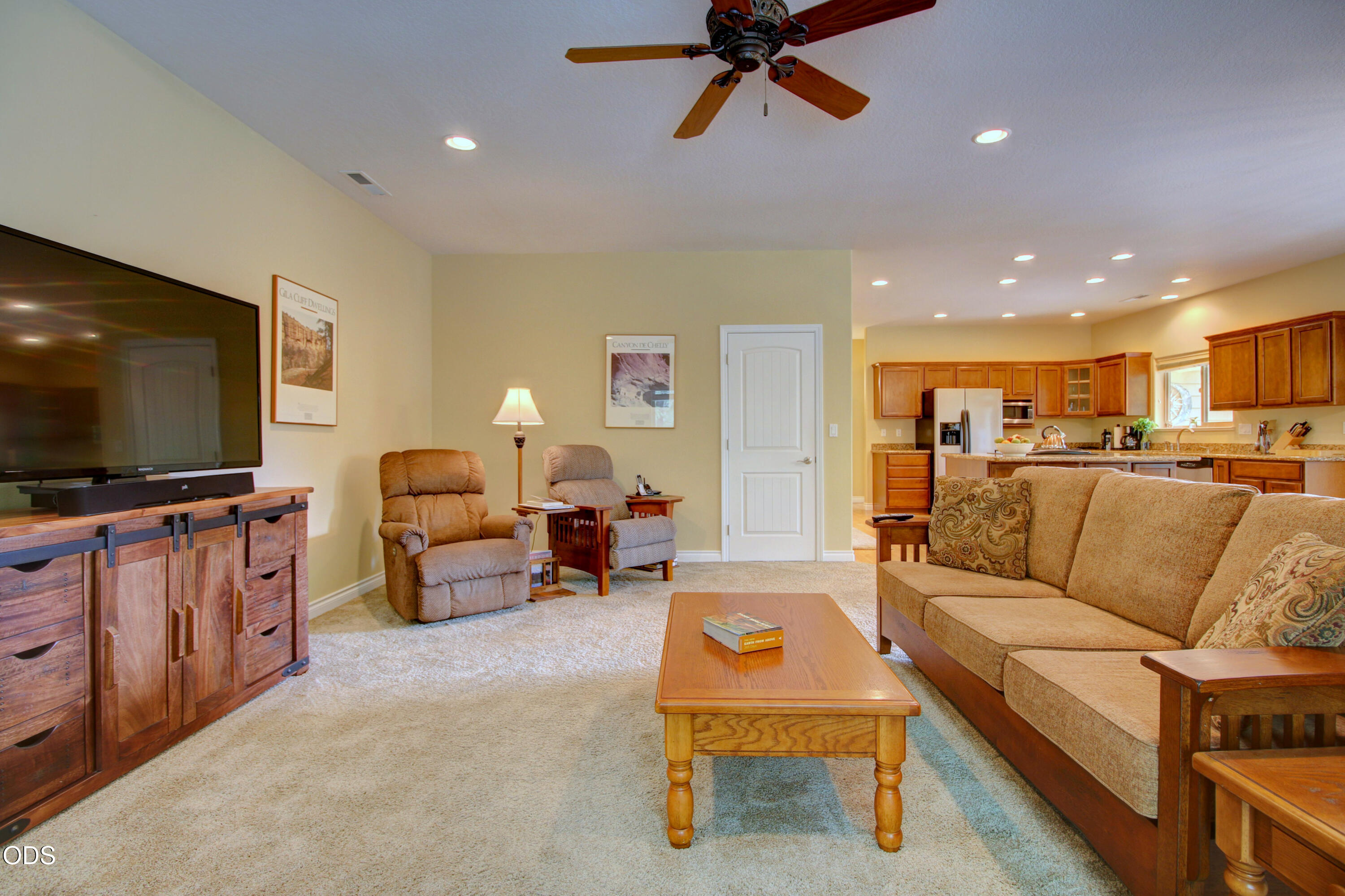 Living room with a beige sectional and recliners opening into a wood-cabinet kitchen.