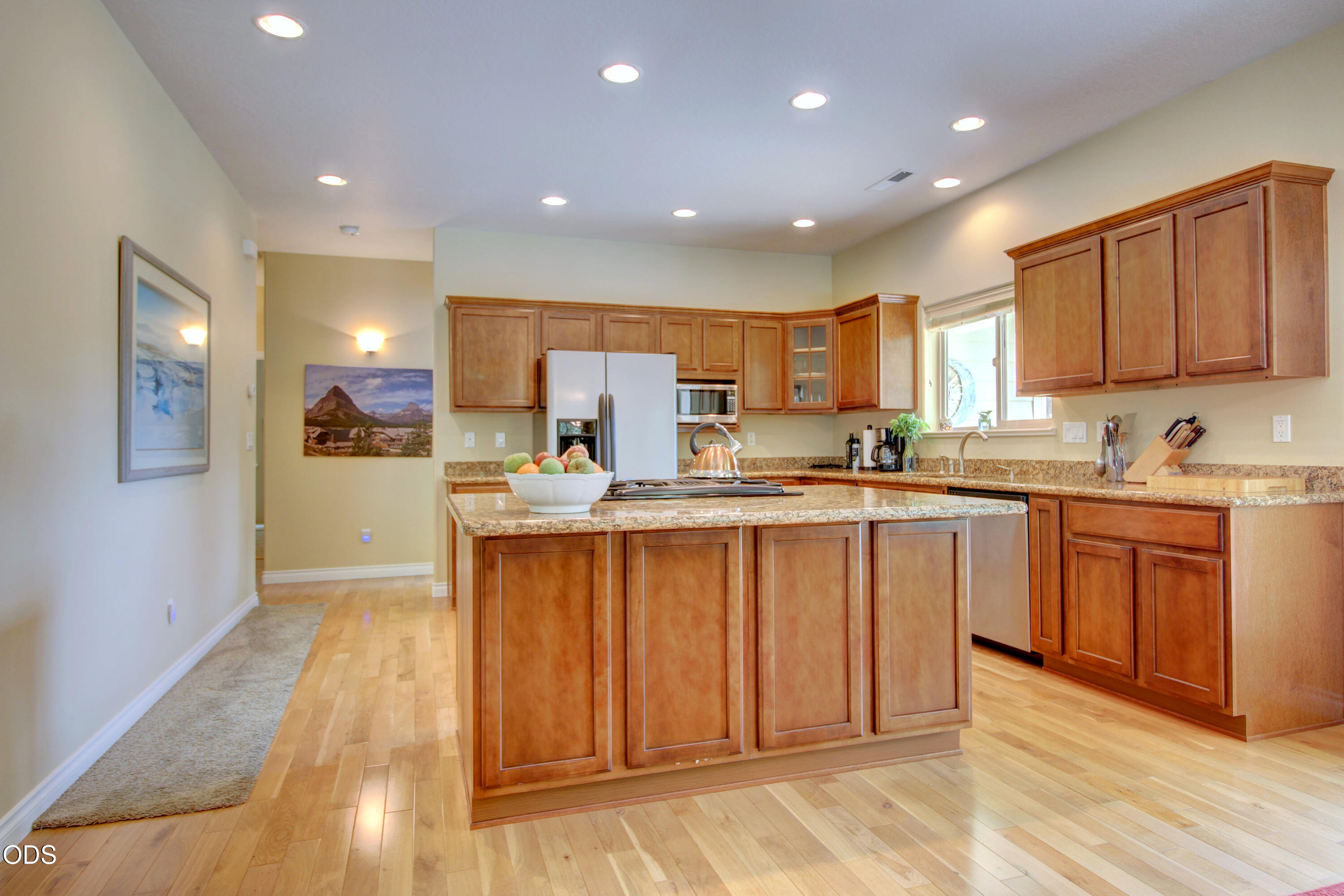 Kitchen with warm wood cabinets, granite island, stainless steel appliances, and light hardwood floors.