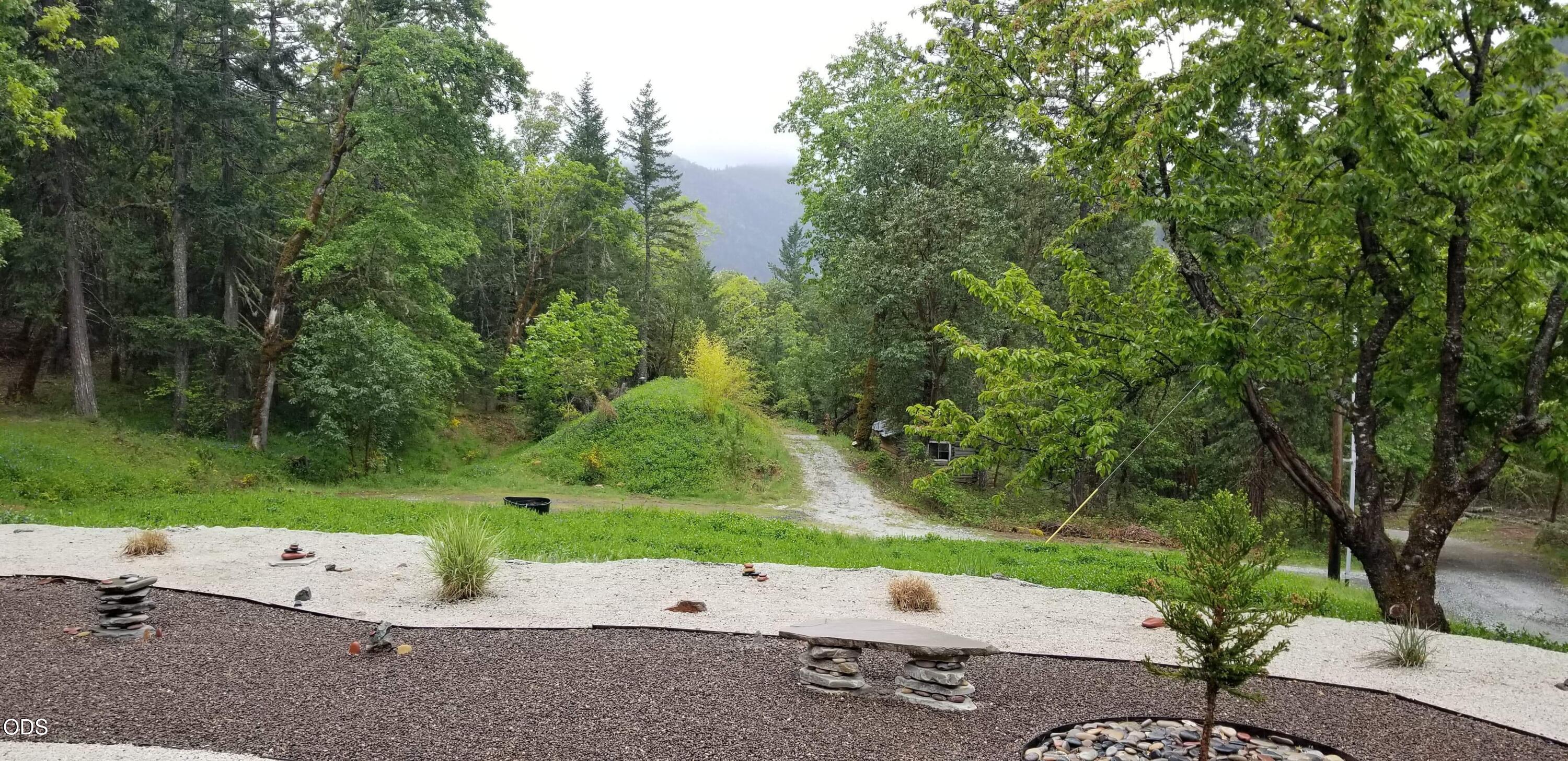 Landscaped yard with a winding gravel drive, dense trees, and a forested mountain view.