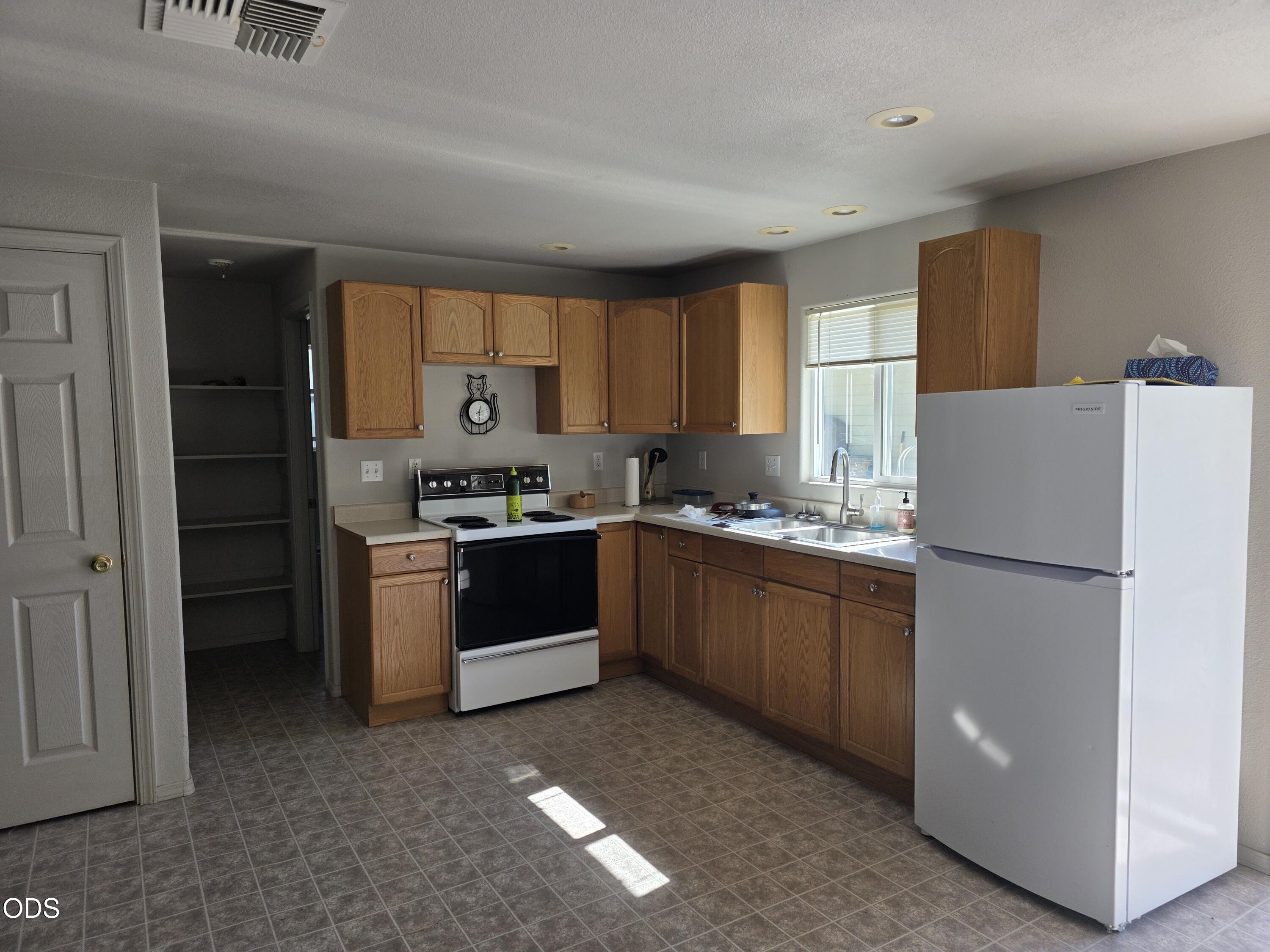 Kitchen with wood cabinets, an electric range, double sink, white refrigerator, and open pantry.