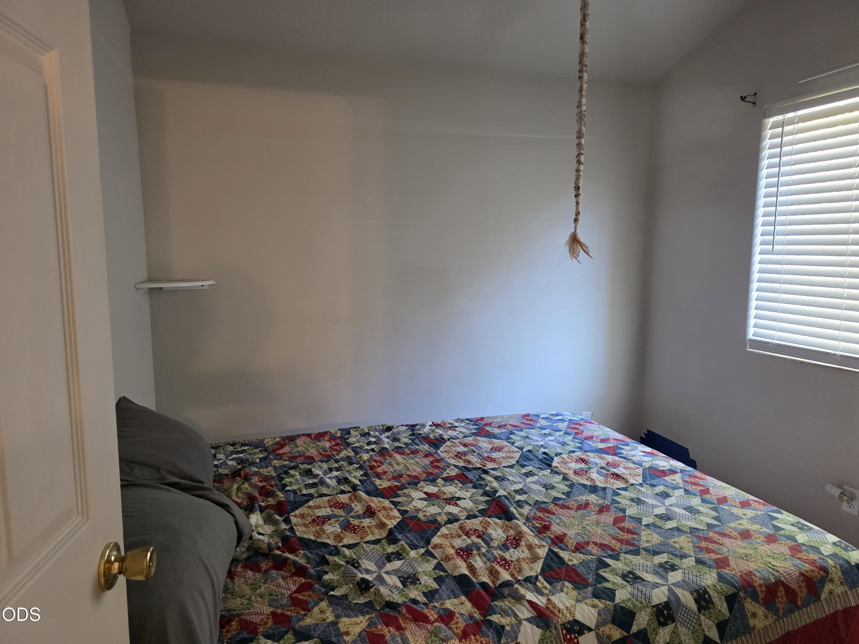 Bedroom with a colorful patchwork quilt on the bed and a window with blinds.