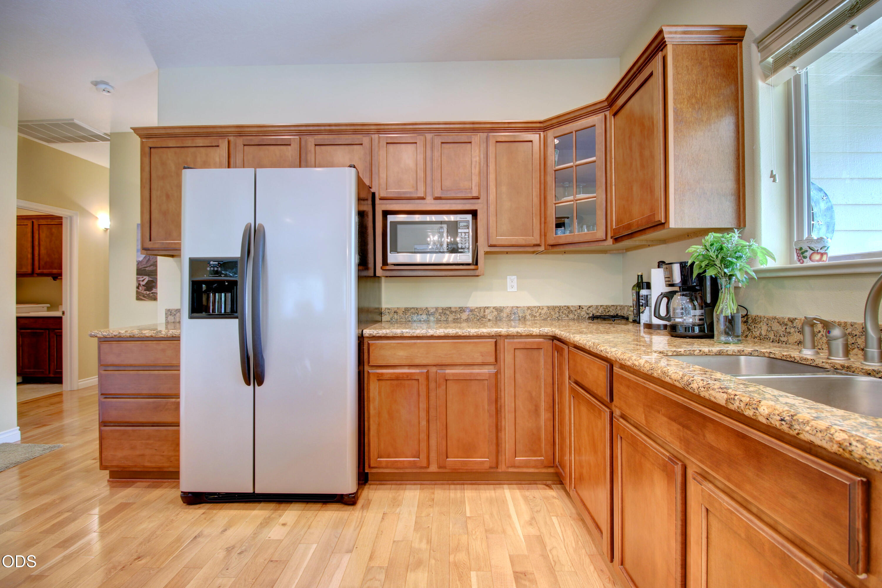 Kitchen with warm wood cabinetry, granite counters, a large white refrigerator, and a double sink beneath a window.