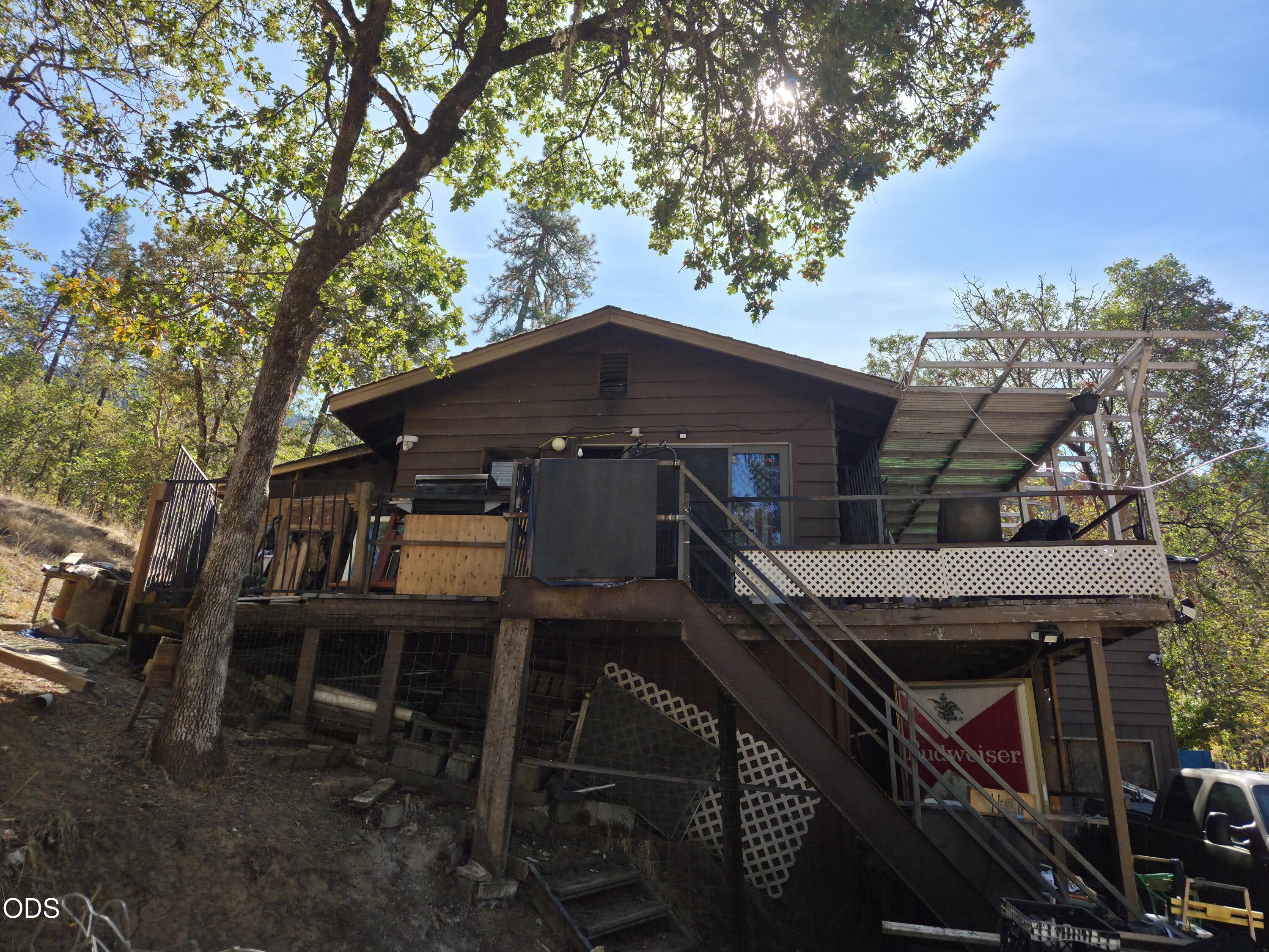 Elevated brown house on a wooded hillside with a raised deck and long exterior stairs.