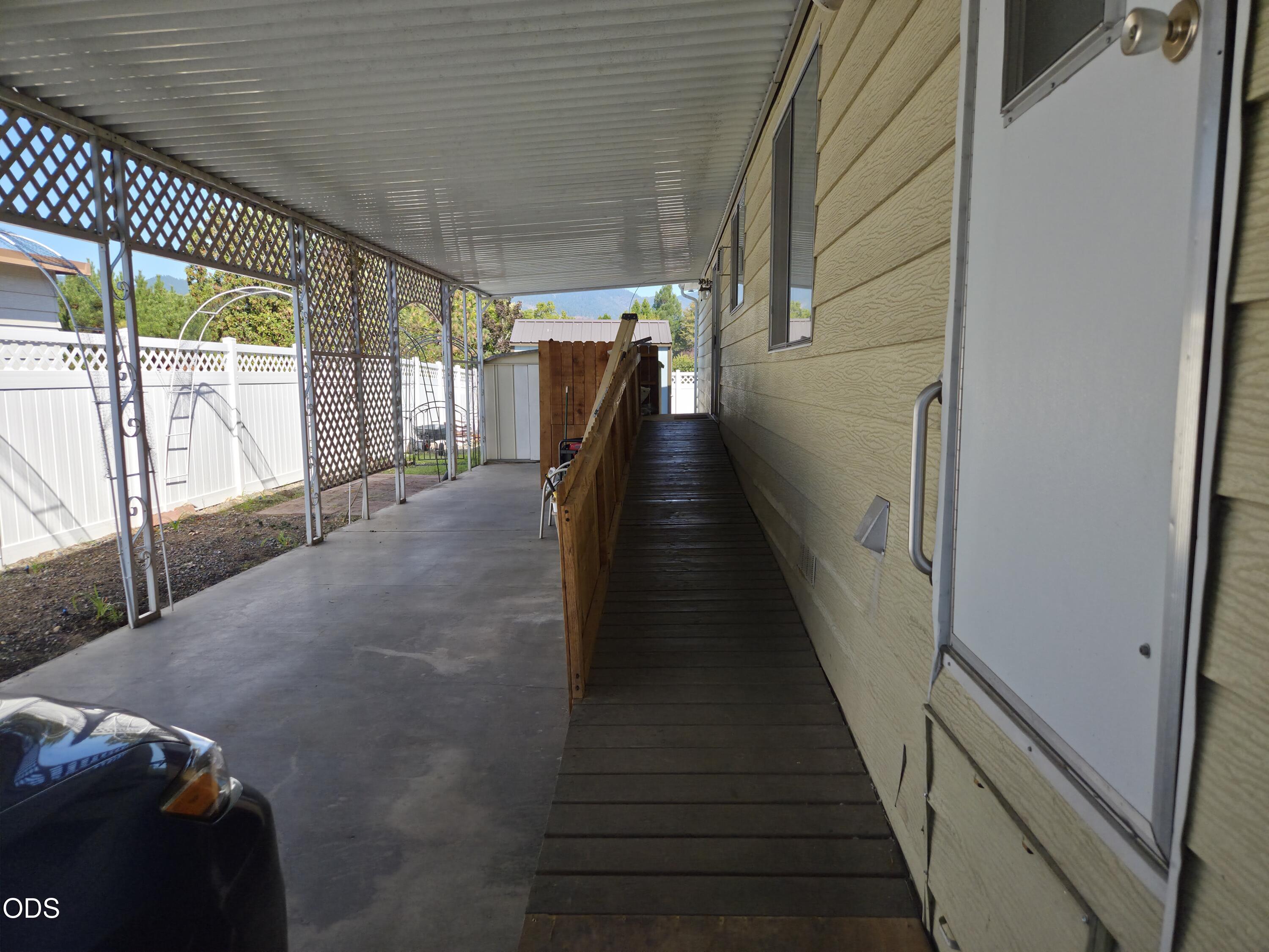 Covered side patio with a wooden accessibility ramp beside the home.