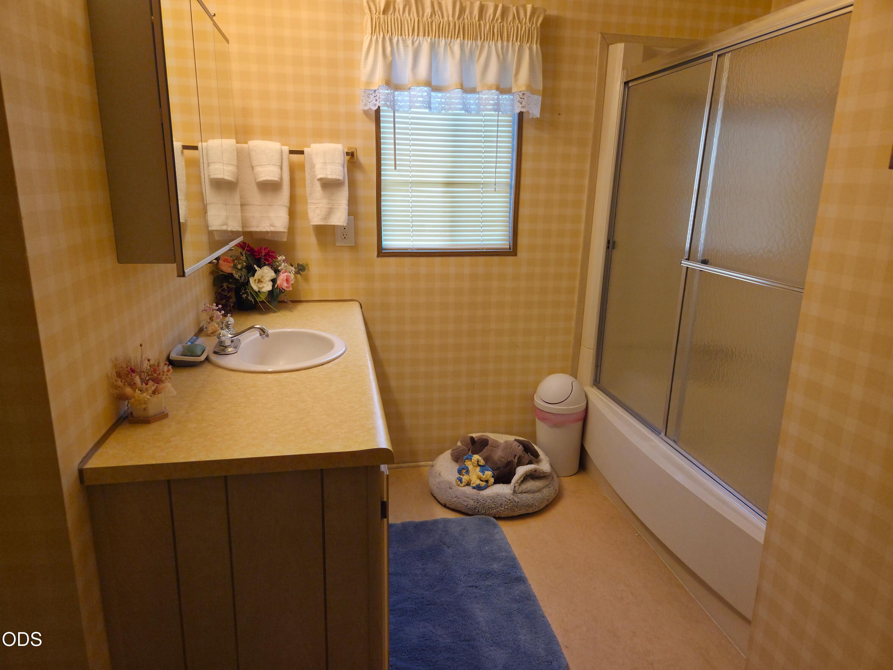 Bathroom with a vanity sink, window, and sliding-glass tub and shower.