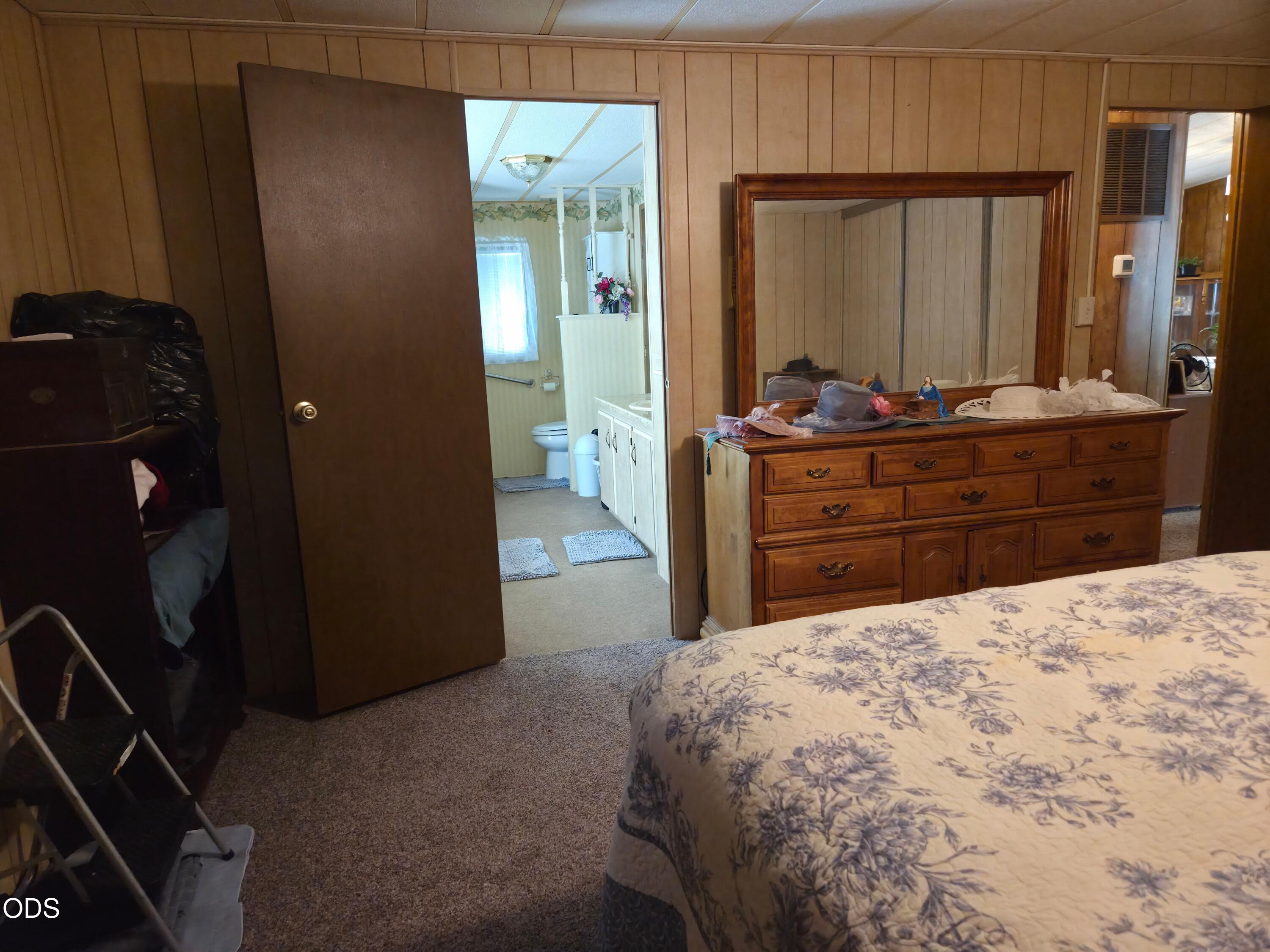 Bedroom with a floral quilt, wooden dresser and mirror, and an open doorway to the bathroom.