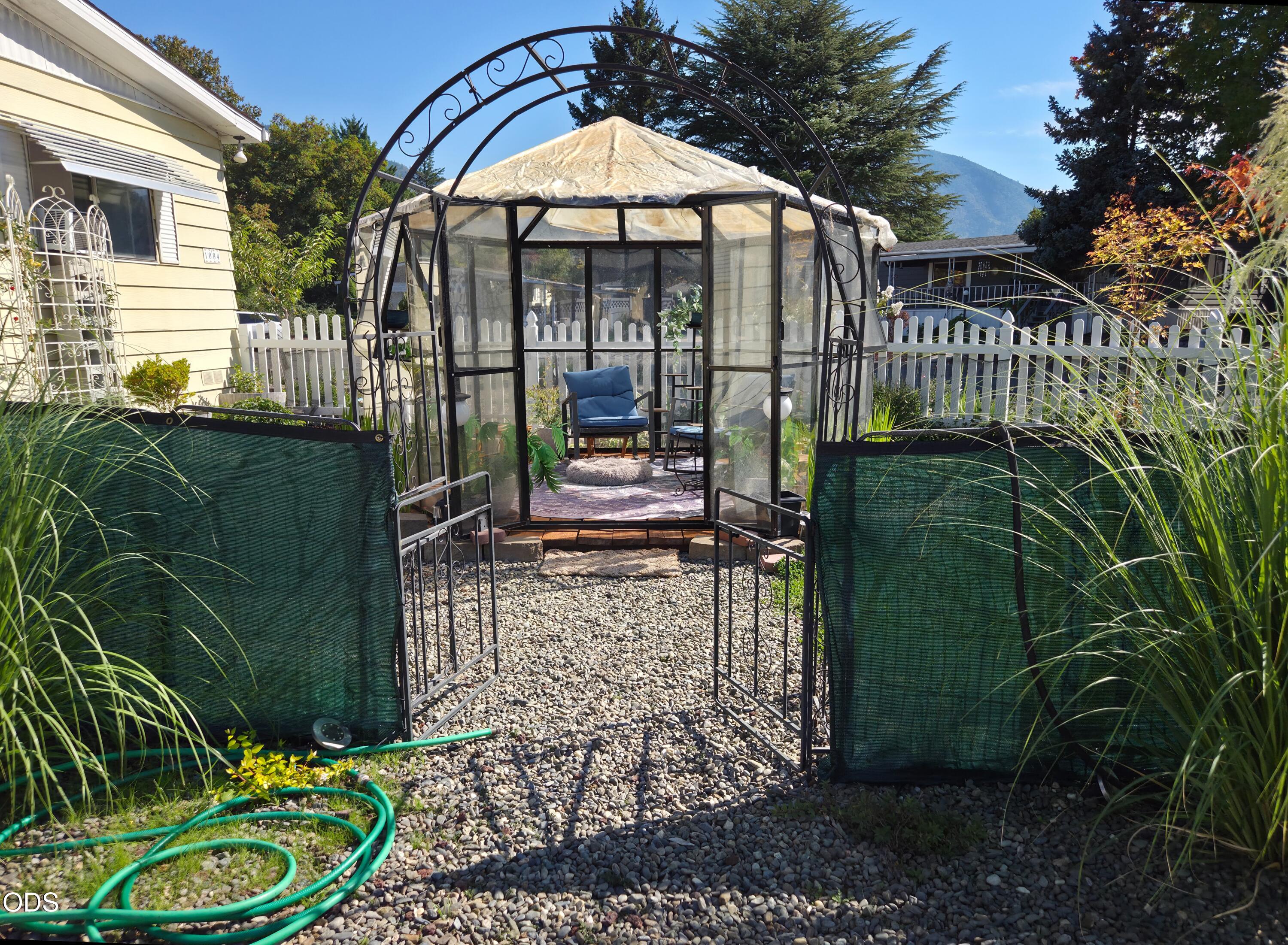 Garden gazebo with blue seating, reached by a gravel path through an arched gate.