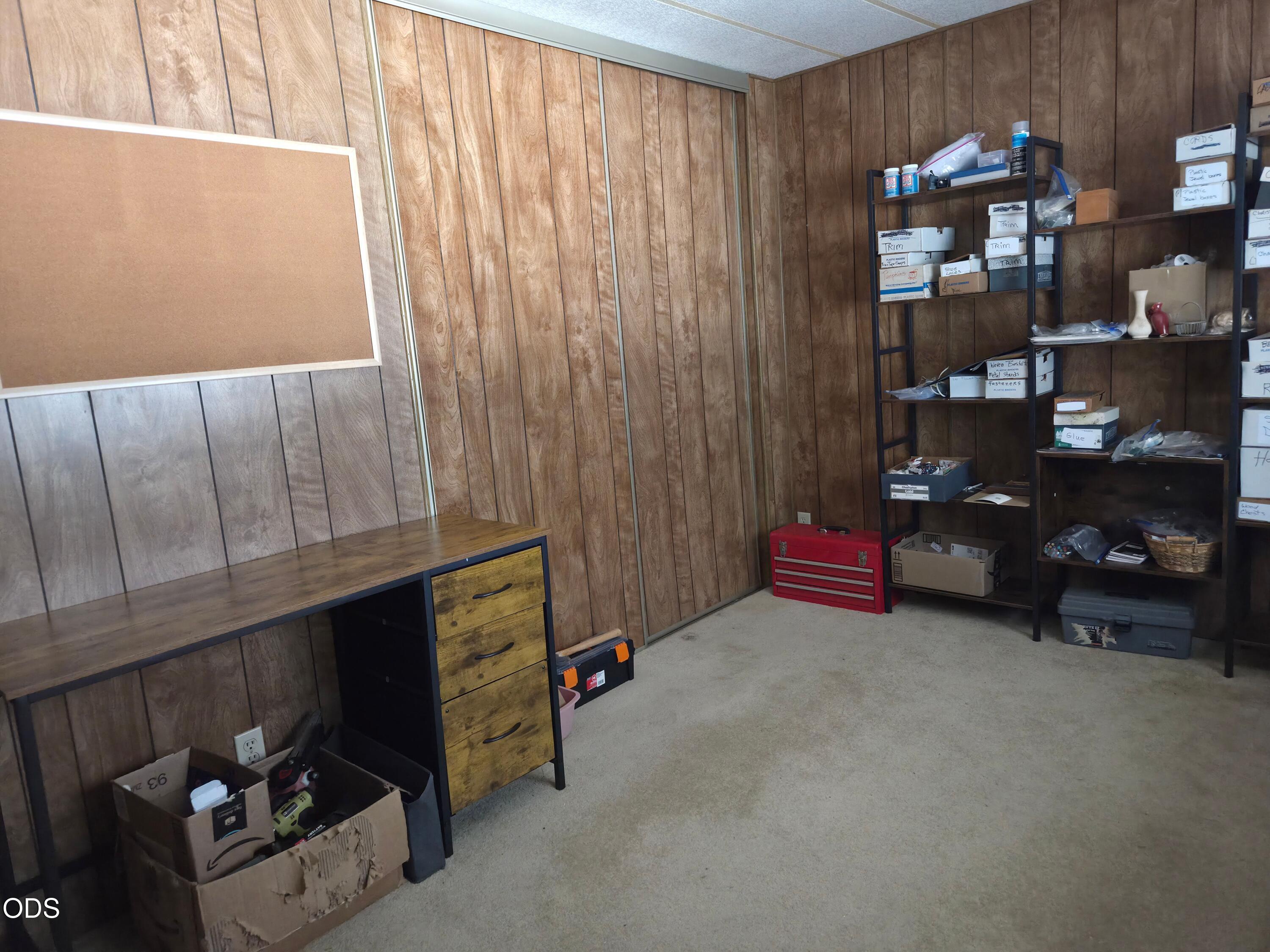 Workshop with wood-paneled walls, a workbench, and shelves of tools and supplies.