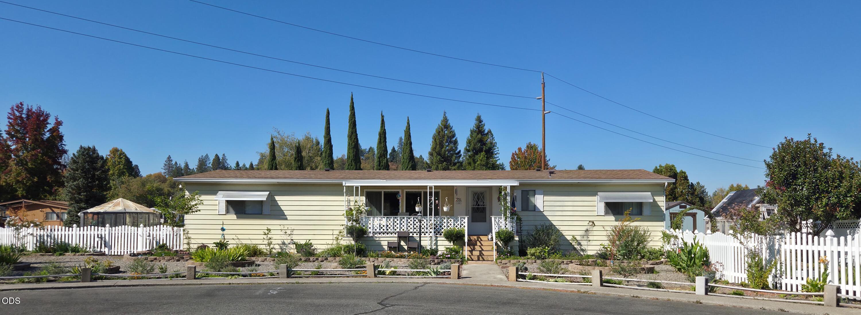 Single-story pale green home with a white picket fence and landscaped front yard.