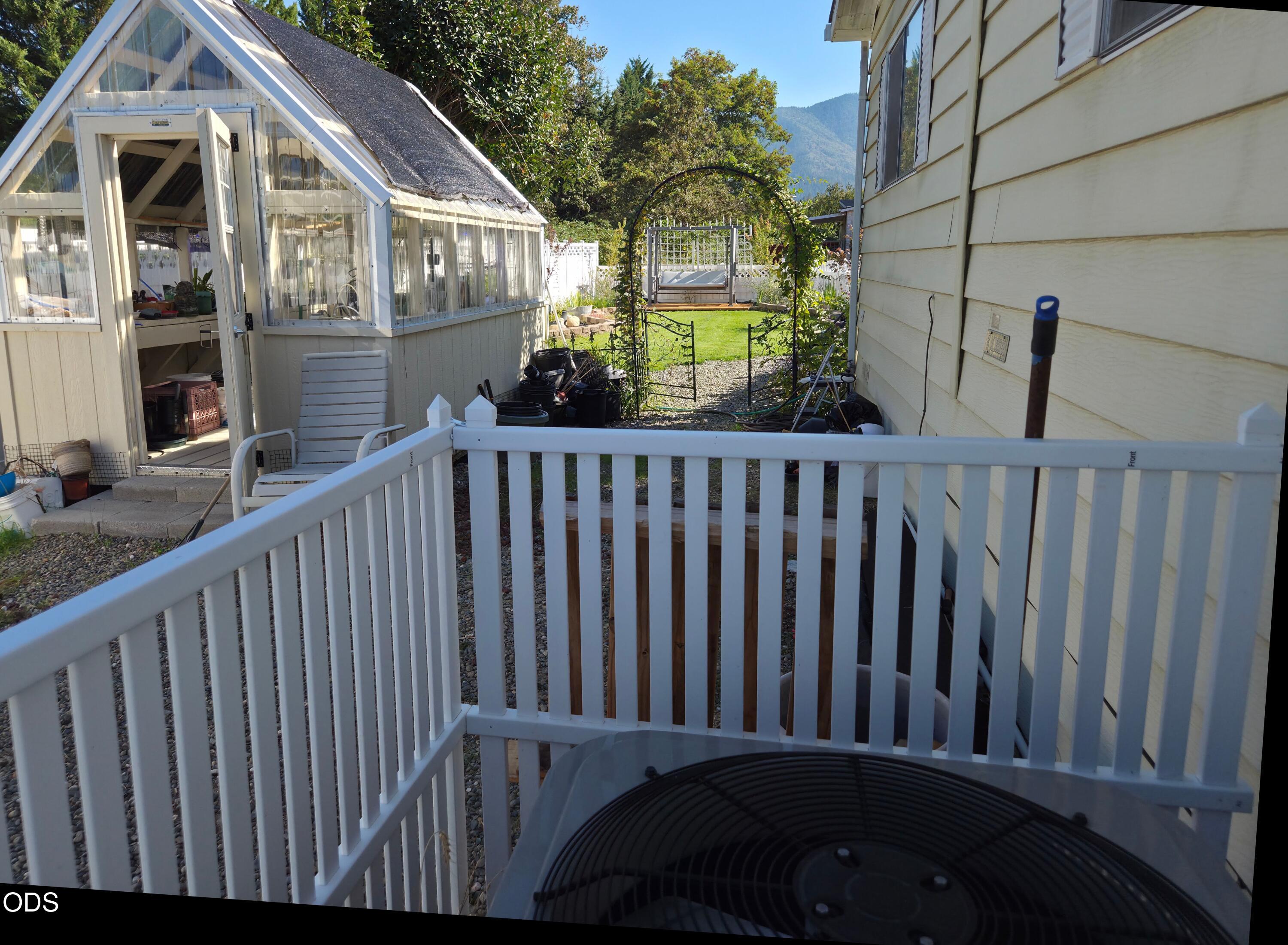 Side yard with a glass greenhouse, garden arch, and lawn behind white deck railings.