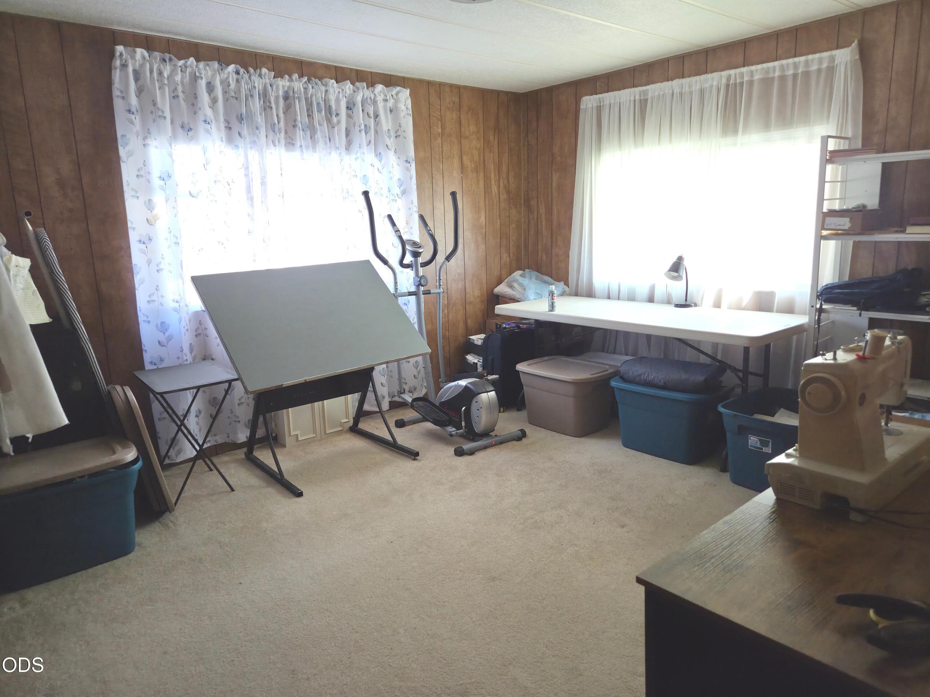 Carpeted room with wood-paneled walls, exercise equipment, a drafting table, and storage bins.