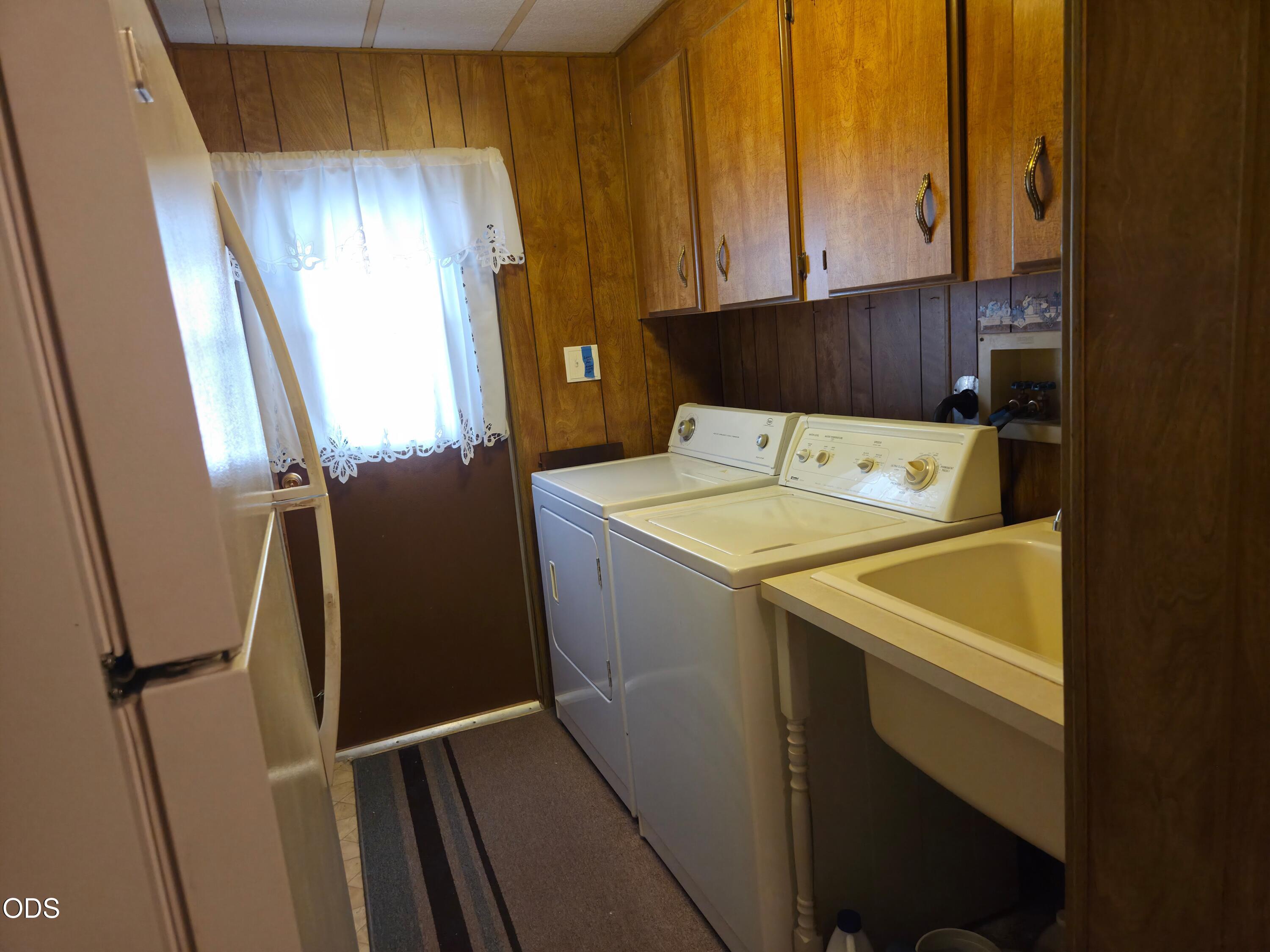 Laundry room with washer, dryer, utility sink, and wood cabinets.
