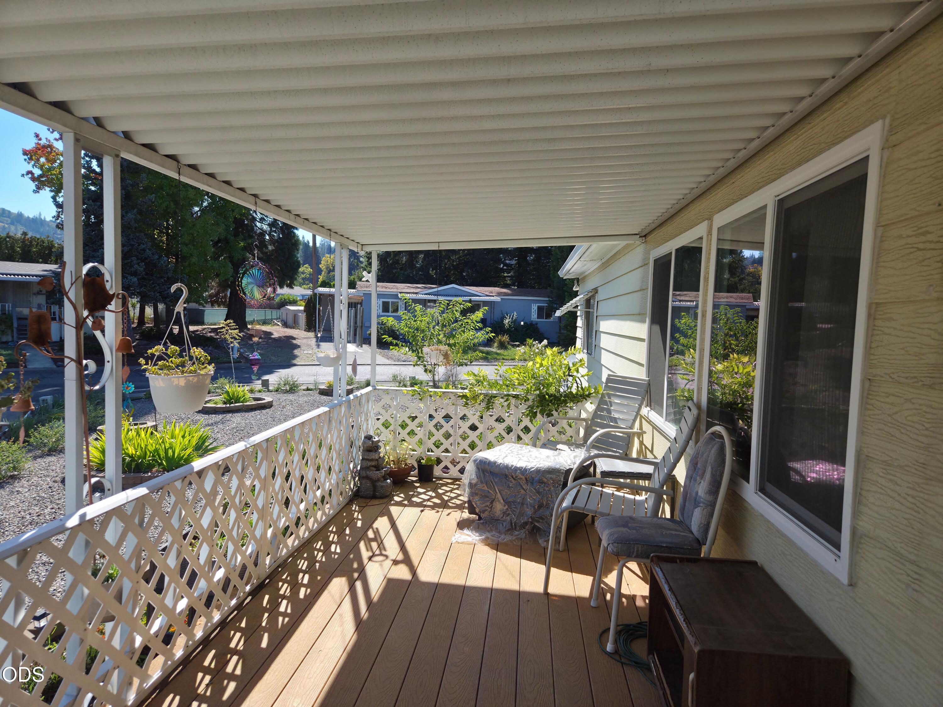 Covered porch with lattice railing, patio chairs, and views of neighboring homes and trees.