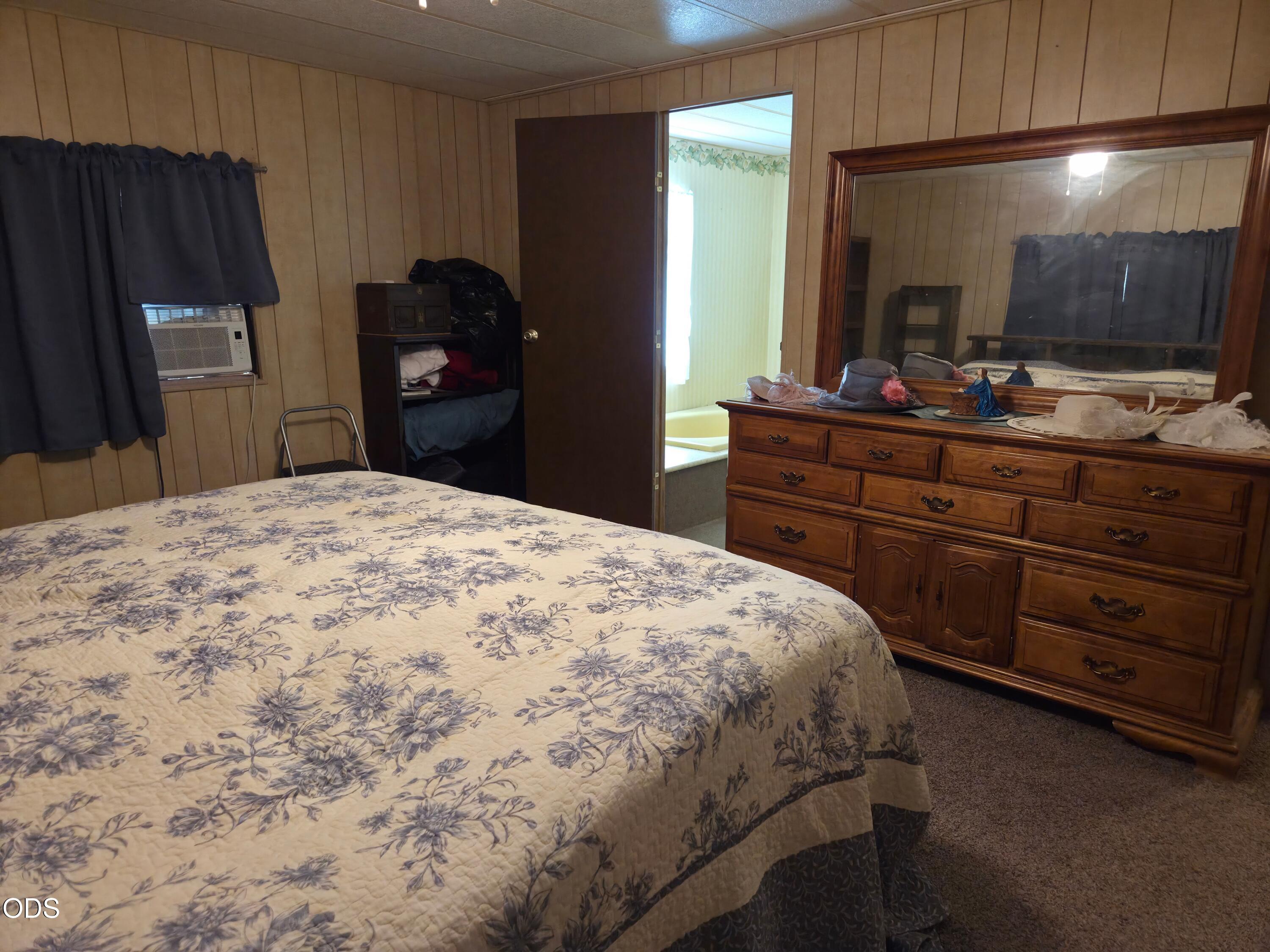 Bedroom with a floral bedspread, large wooden dresser, and doorway to an adjoining bathroom.