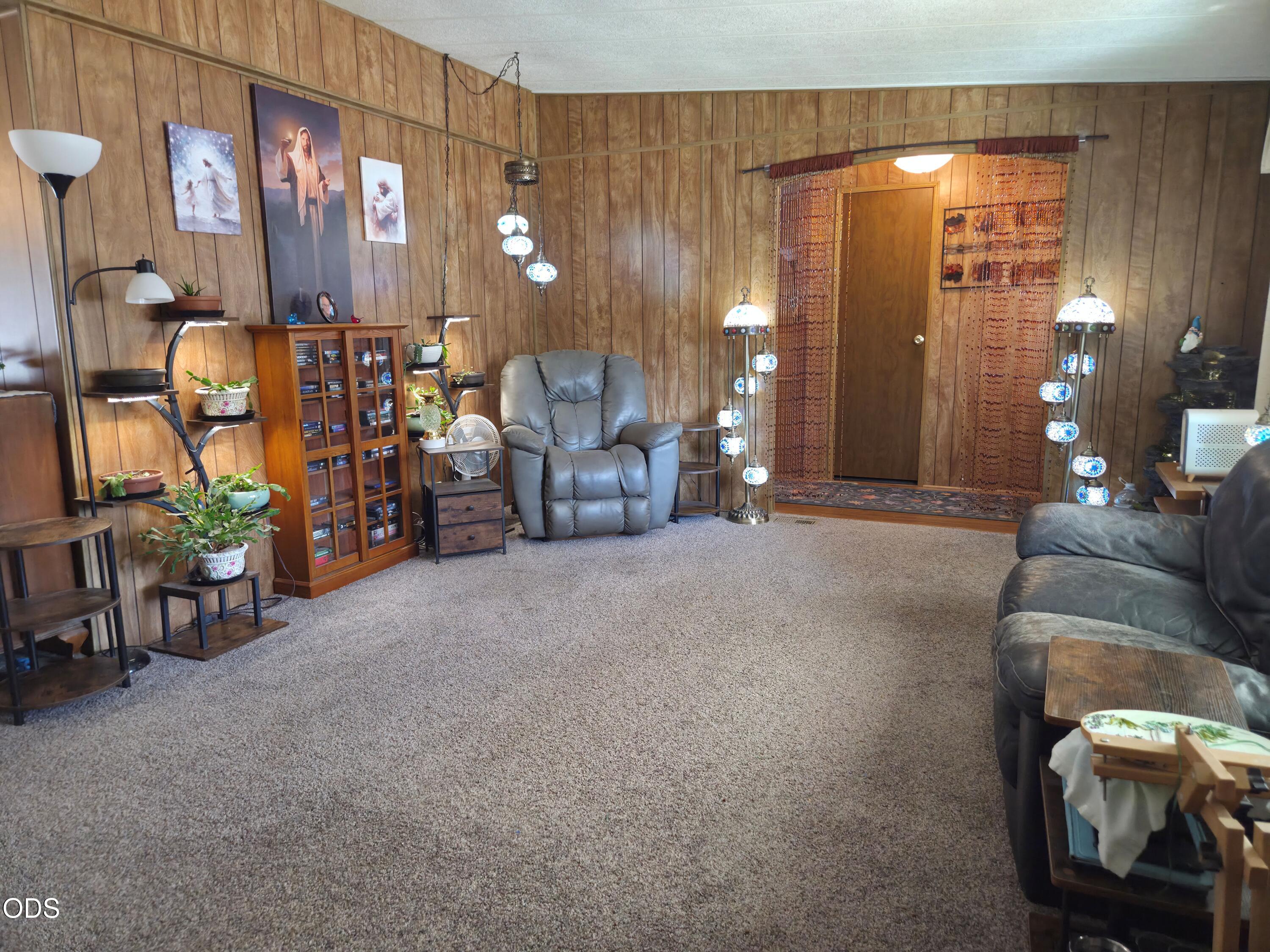 Wood-paneled living room with gray recliners, carpet, a media cabinet, and decorative pendant lights.