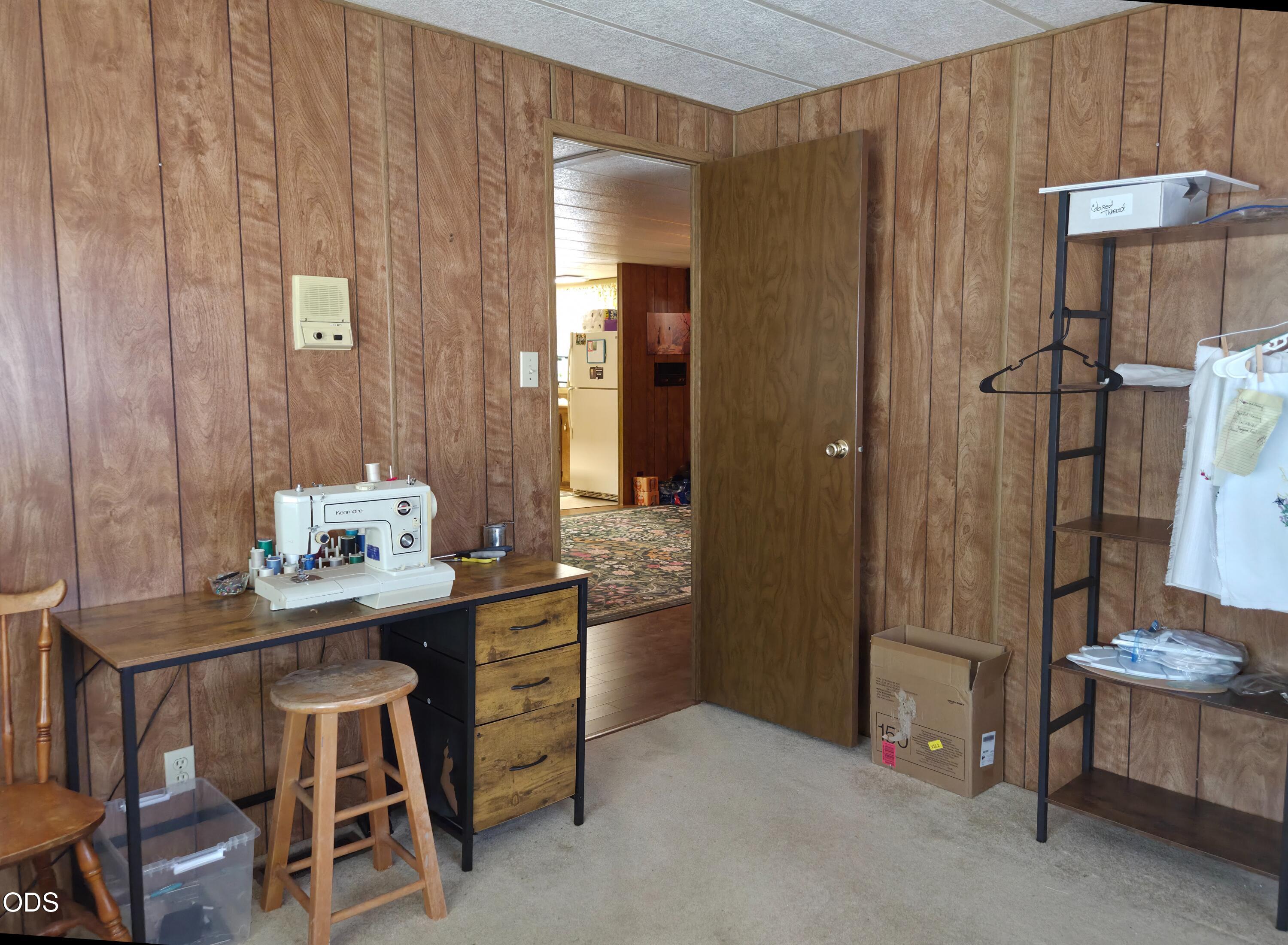 Sewing room with a Kenmore machine on a desk, wood-paneled walls, and open storage shelving.