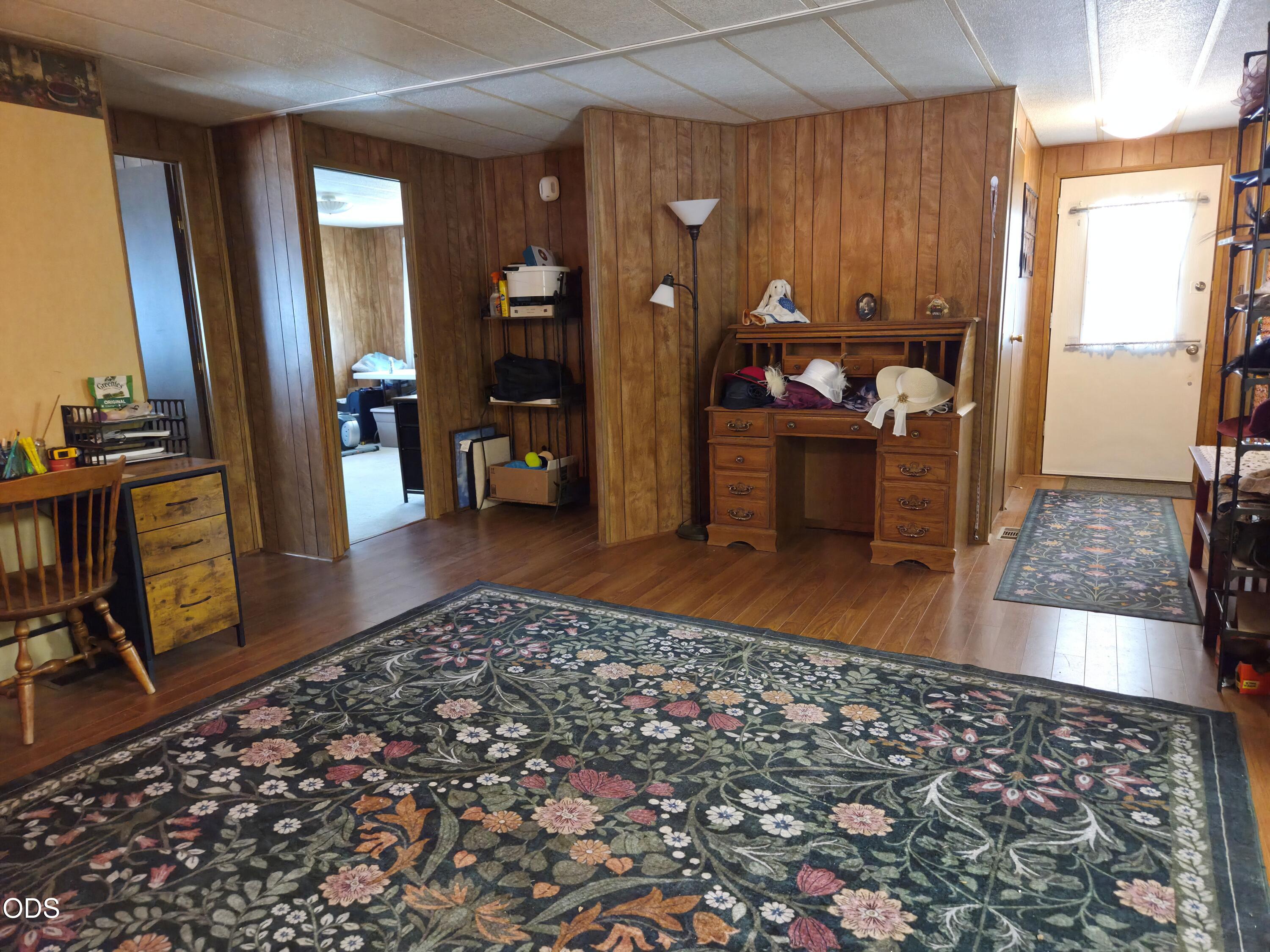 Wood-paneled entry room with a floral rug, vintage desk, and front door.