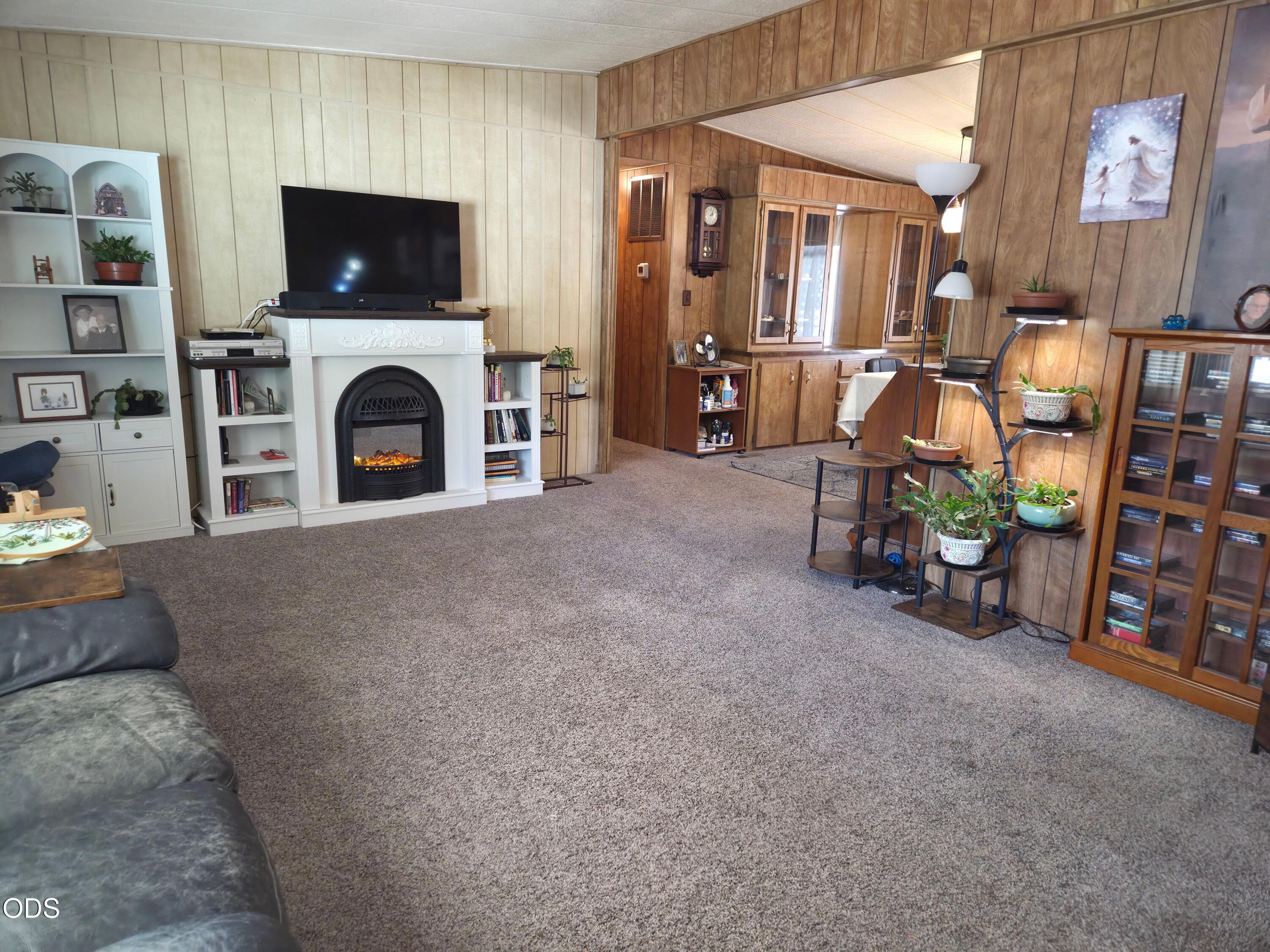 Living room with a white fireplace, built-in shelves, wood-paneled walls, and carpet.