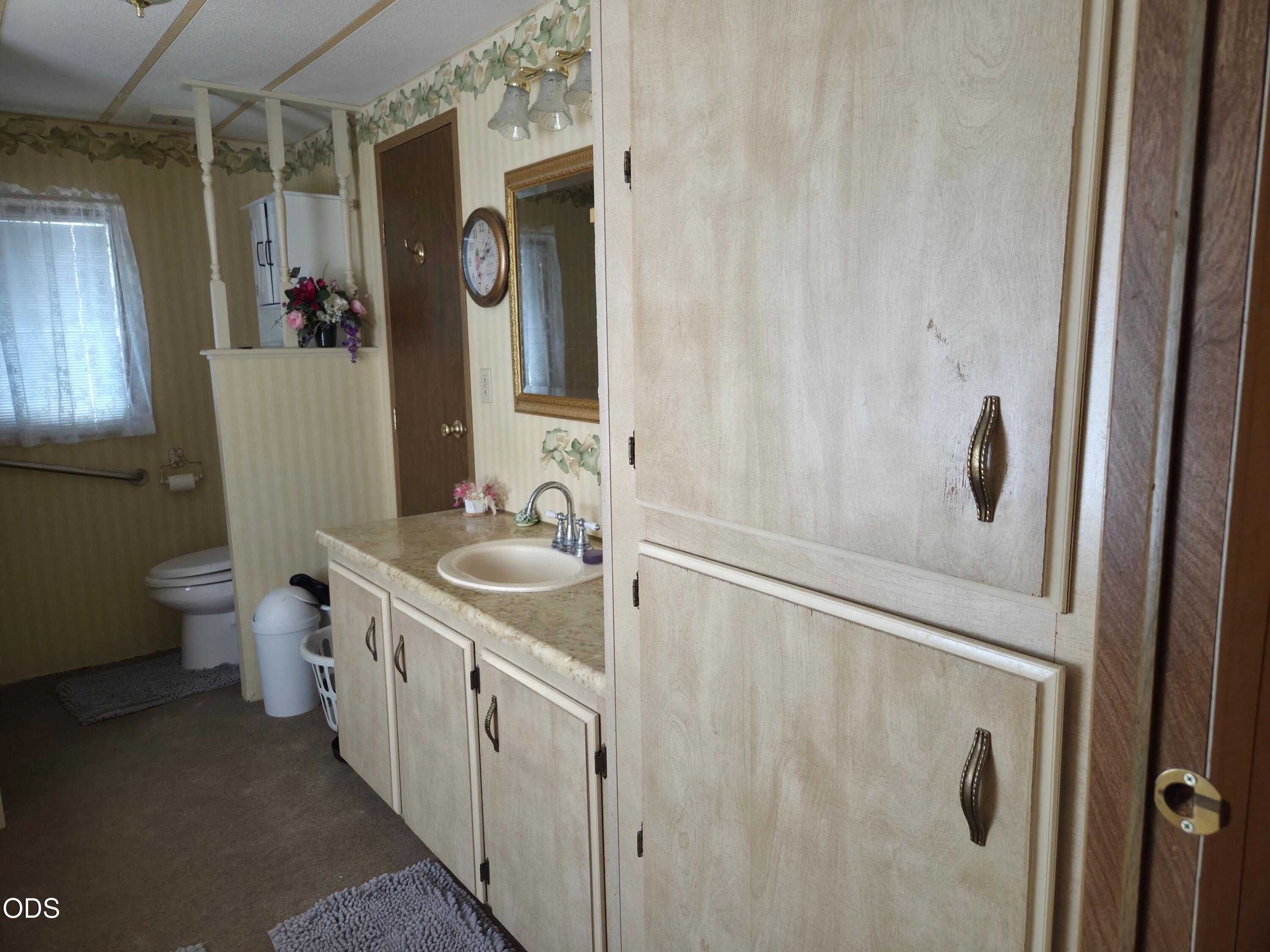 Bathroom with a long vanity, wall mirror, and toilet behind a half partition.