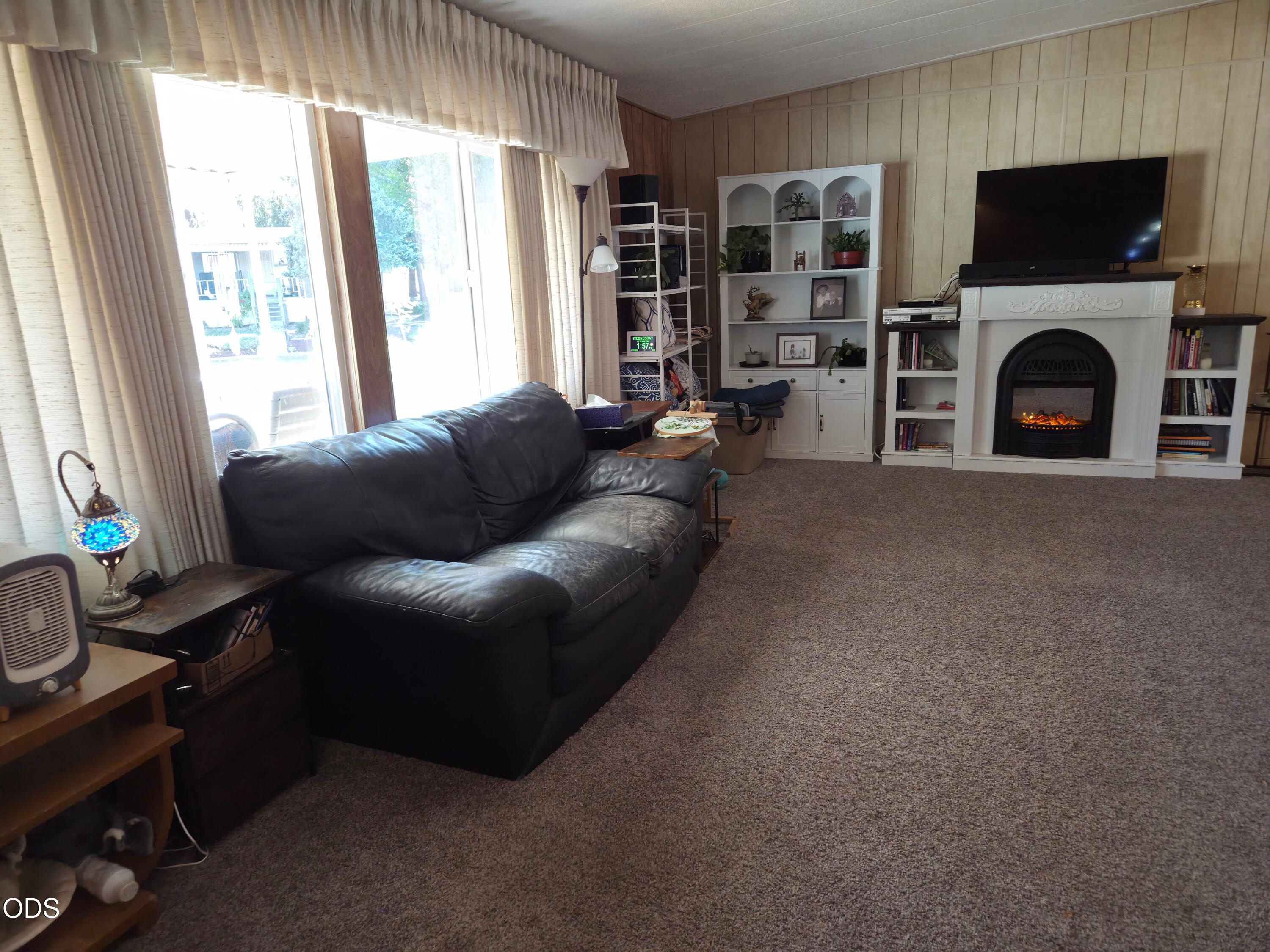 Furnished living room with a black leather sofa, carpet, and white fireplace with built-in shelving.