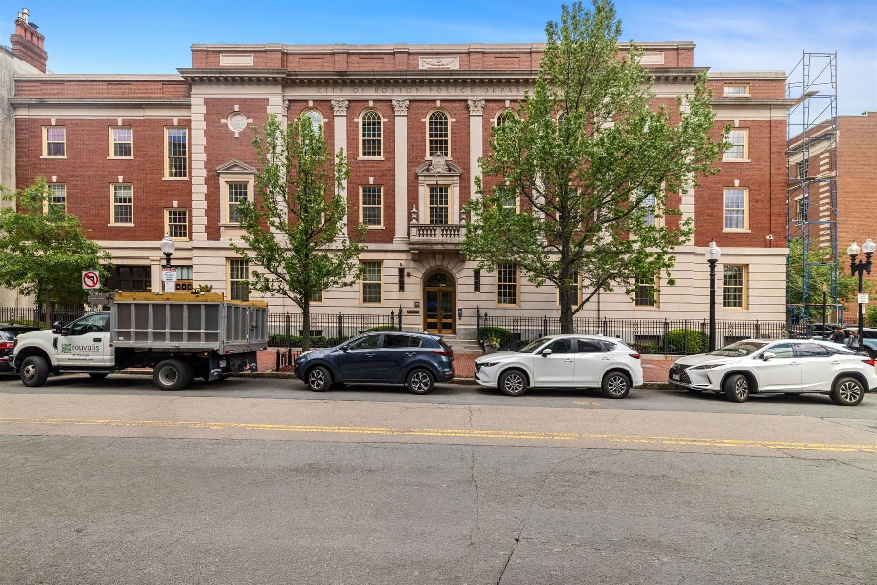 Red-brick Boston Police Department building with arched windows and trees along the sidewalk.