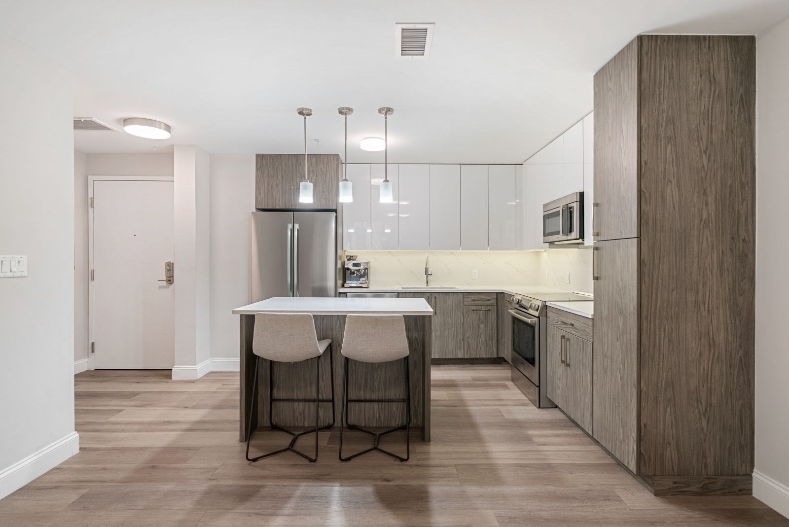 Modern kitchen with gray wood cabinets, stainless appliances, and an island with two stools.