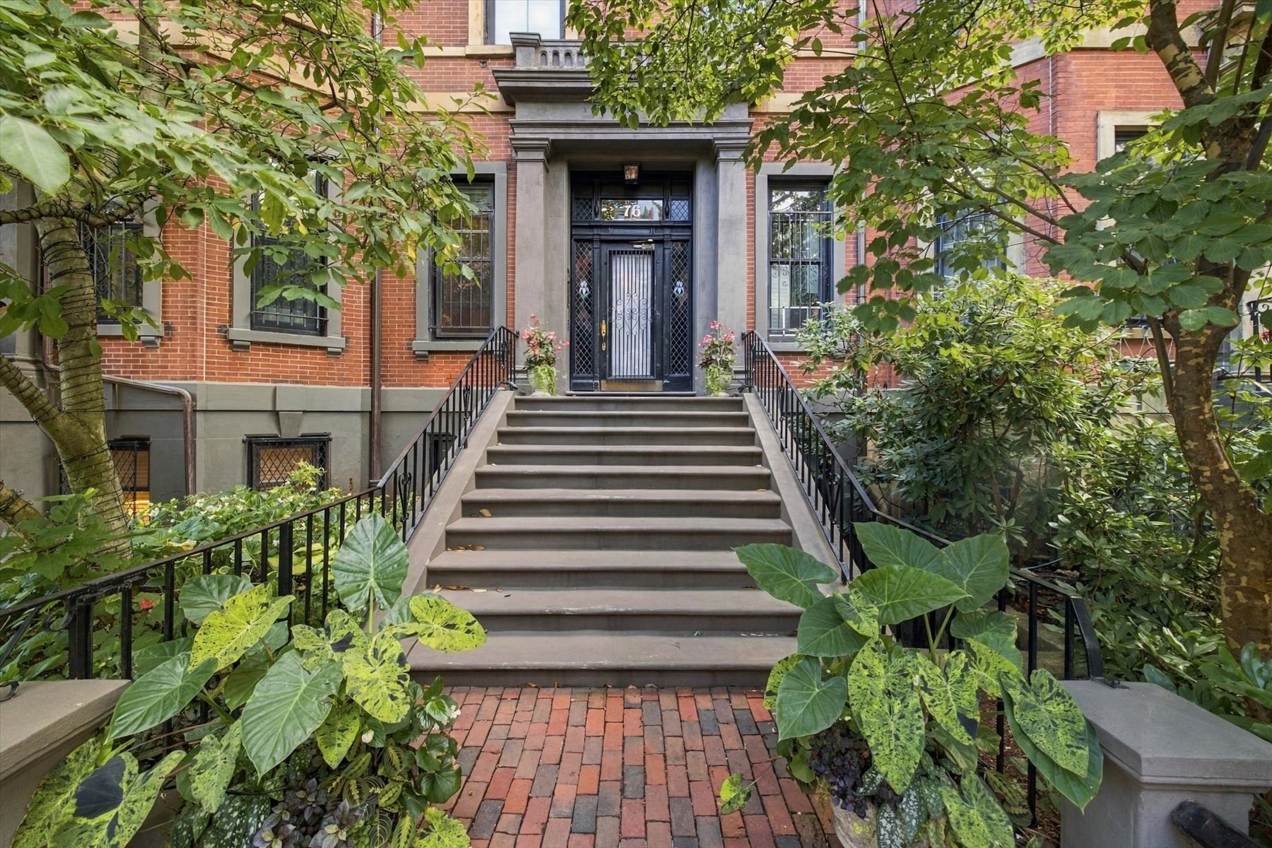 Red-brick residential entrance with broad stone steps, iron railings, and doorway marked 76.