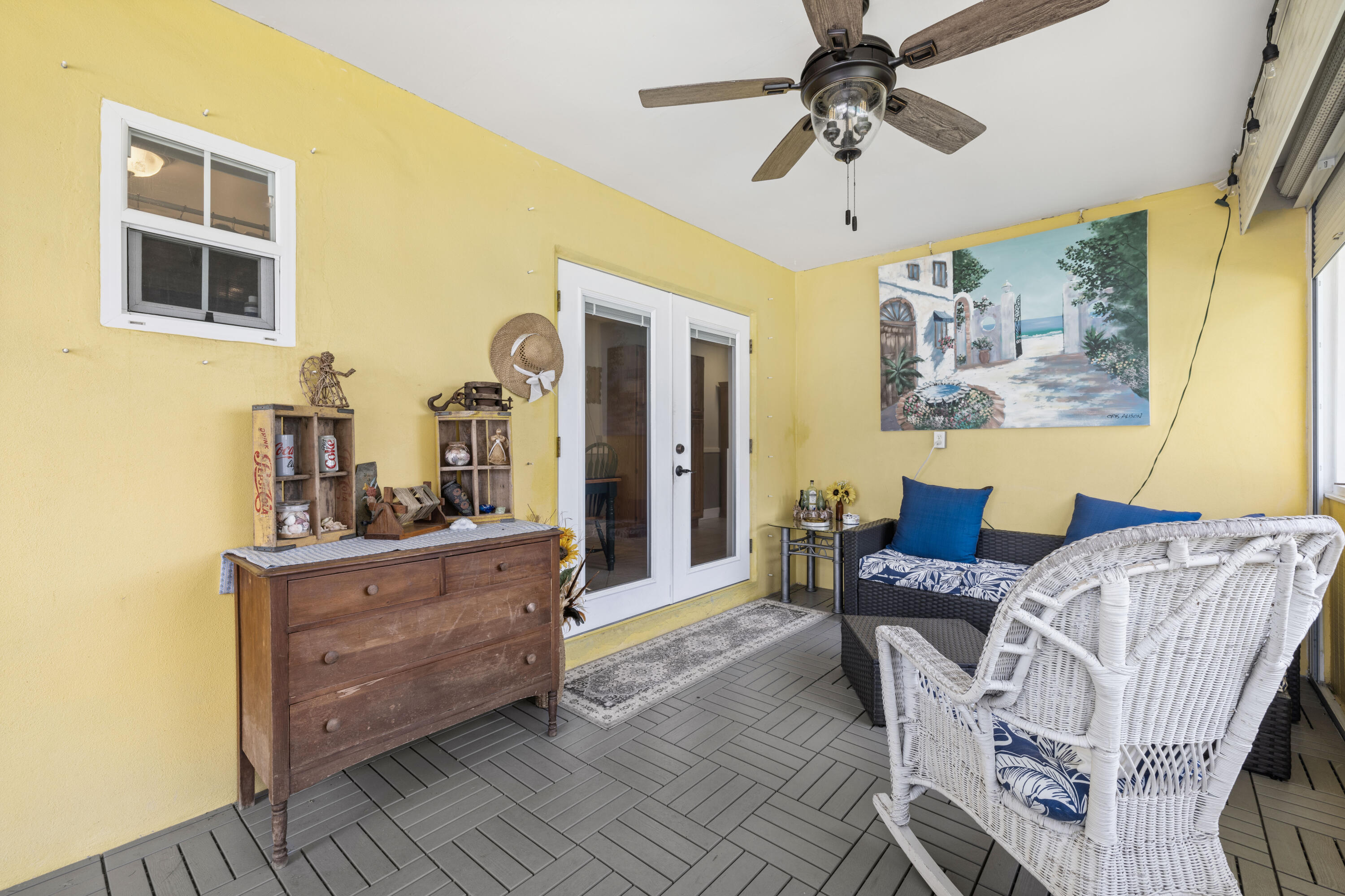 Covered patio with yellow walls, wicker seating with blue cushions, and a ceiling fan.