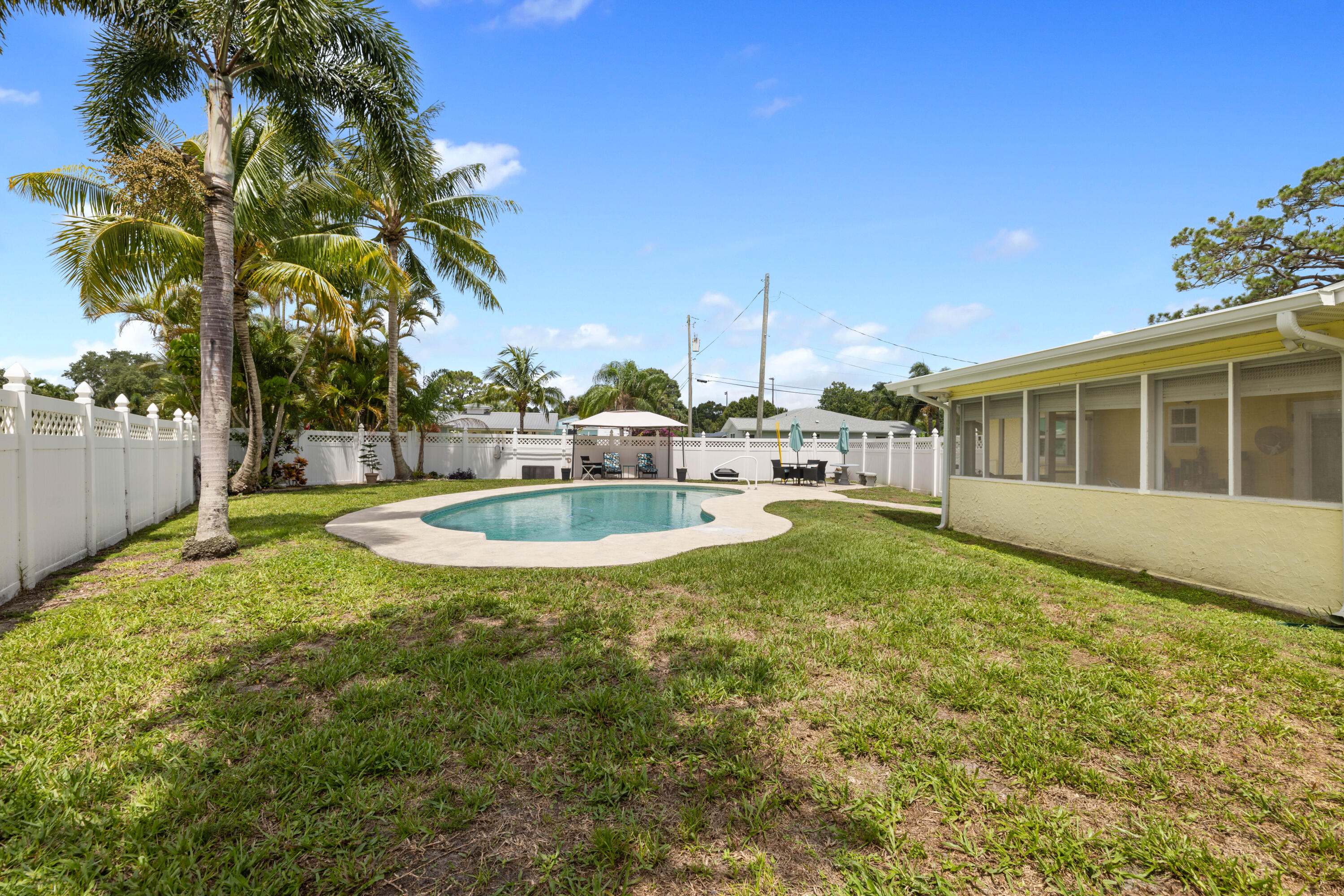 Fenced backyard pool beside a screened porch, with palm trees and patio seating.