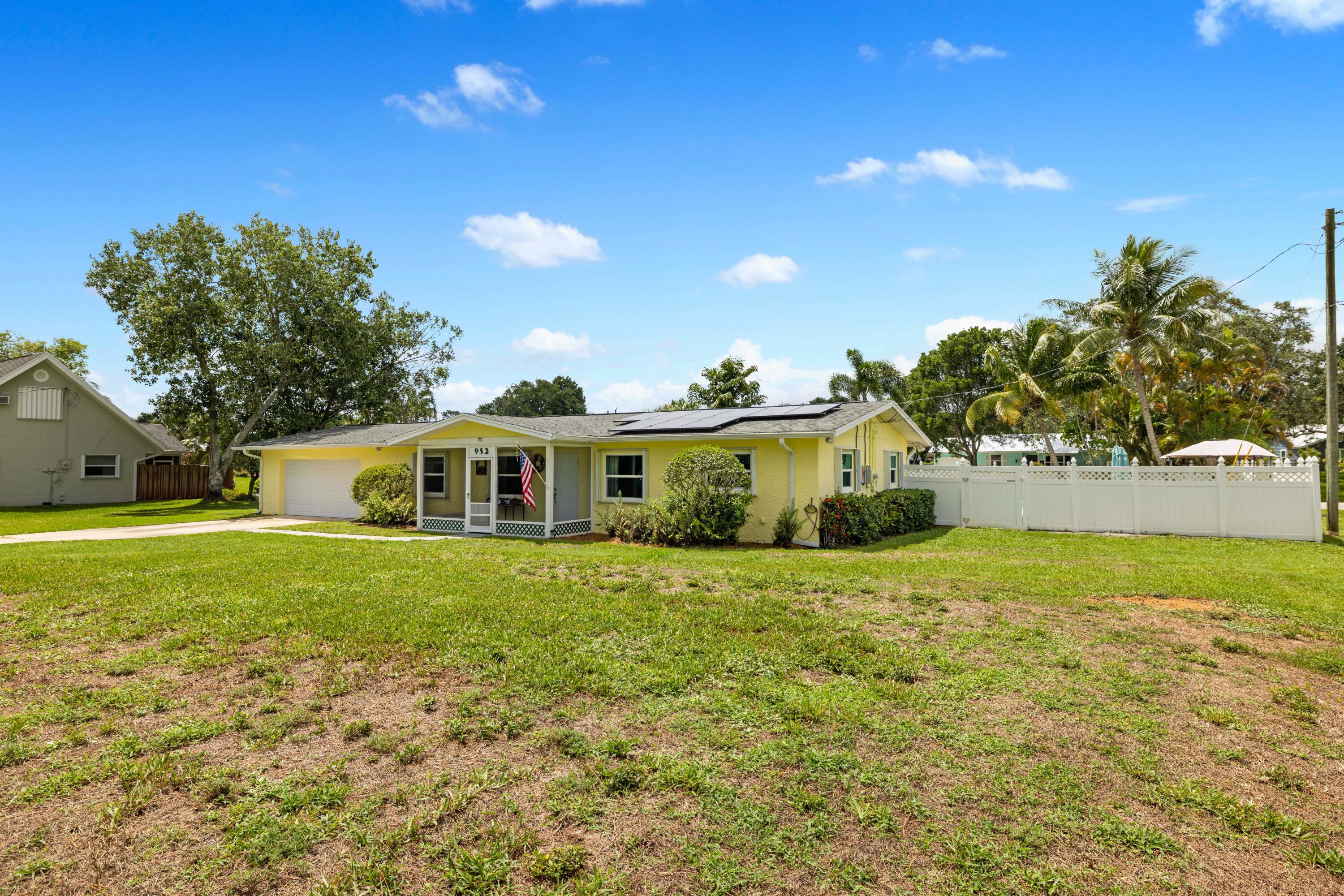 Yellow single-story home with solar panels, attached garage, and white fence.