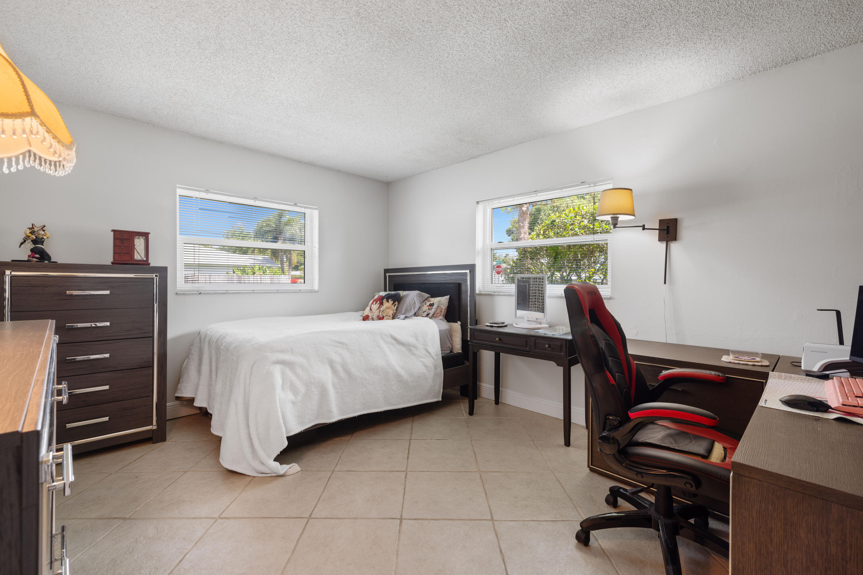 Bedroom with a white-covered bed, dark wood furniture, and a black-and-red gaming chair.