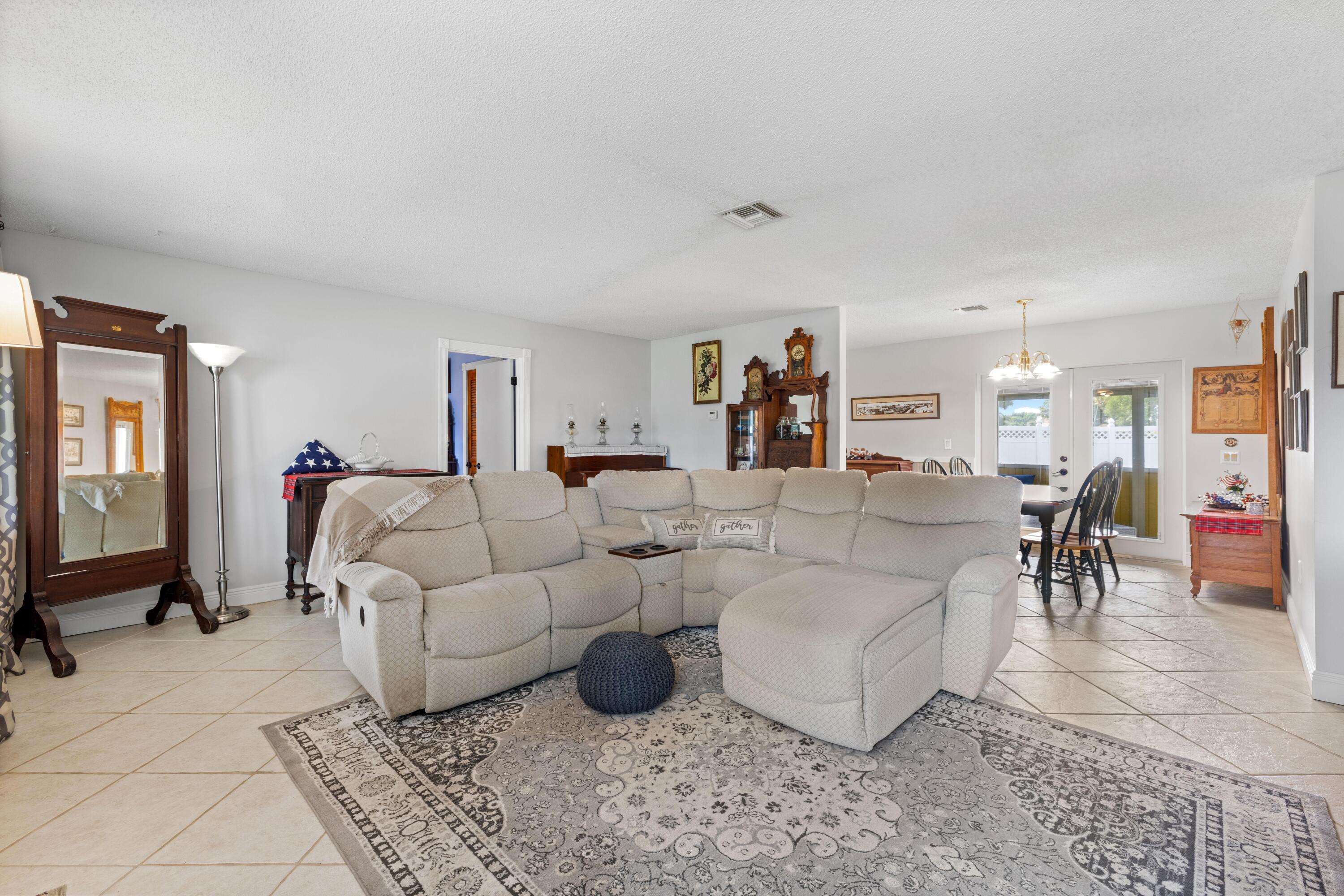 Living room with a cream sectional and chaise, patterned rug, tile floors, and an adjoining dining area.
