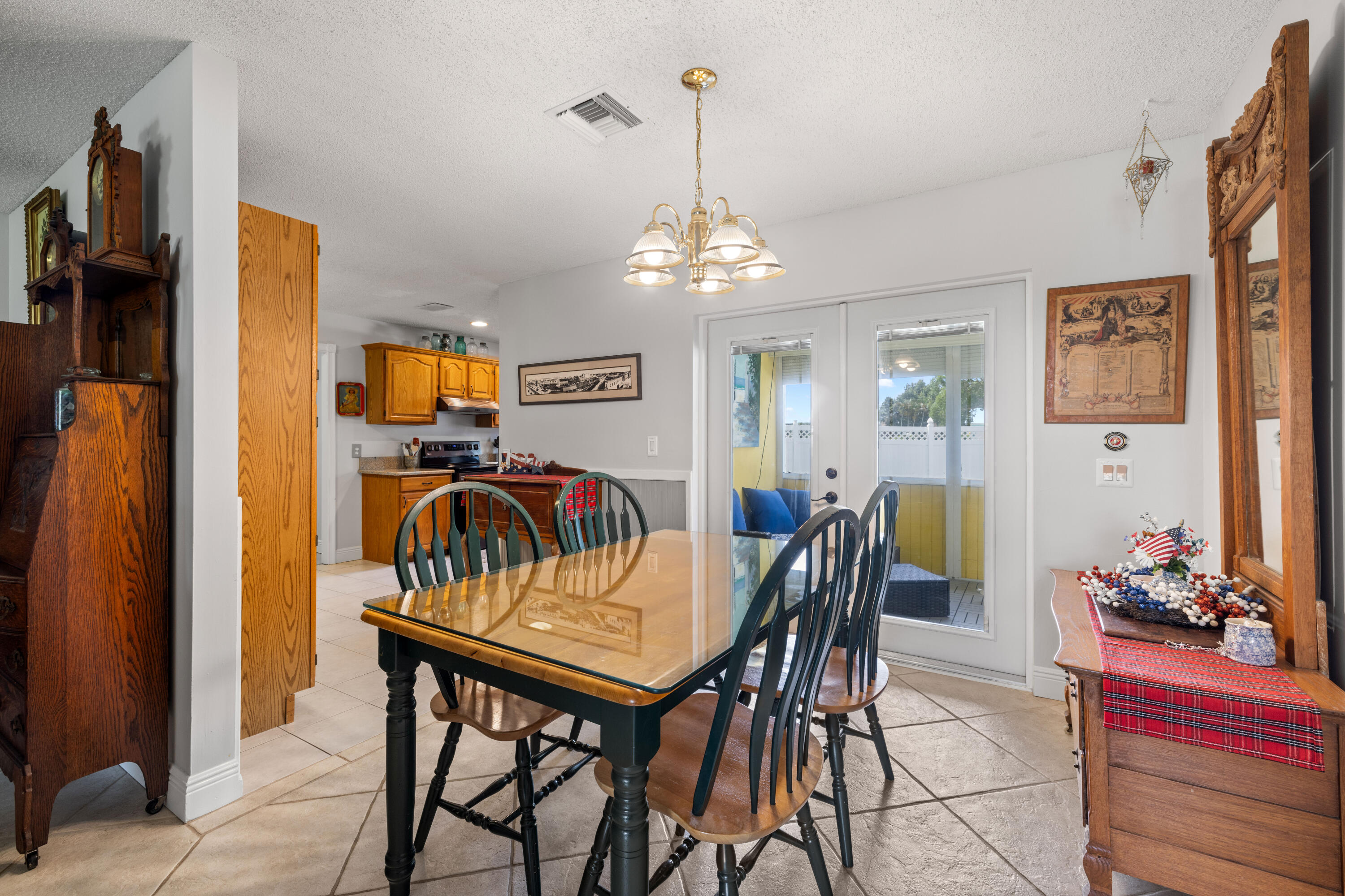 Dining room with a glass-top table and chandelier beside an open kitchen and patio doors.