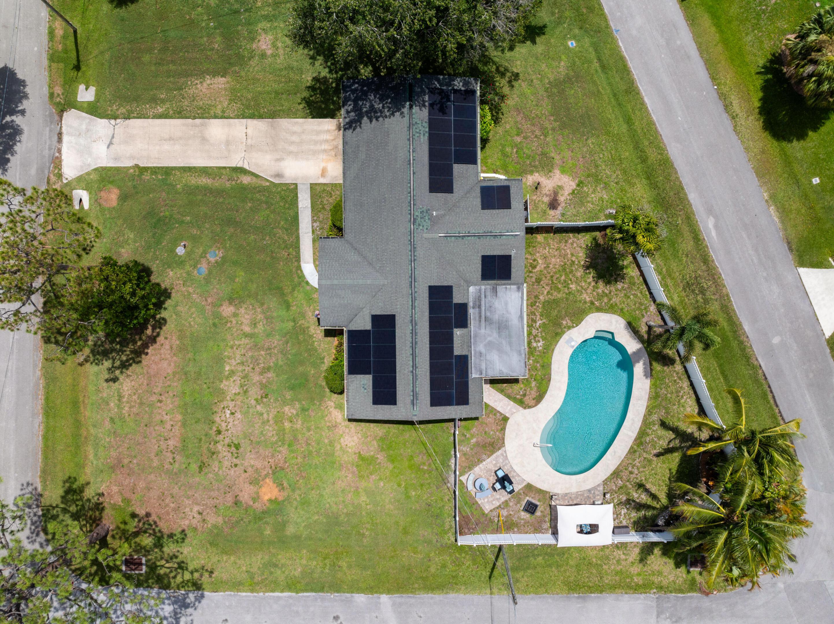 Aerial view of a home with rooftop solar panels, a curved pool, and a spacious grassy yard.