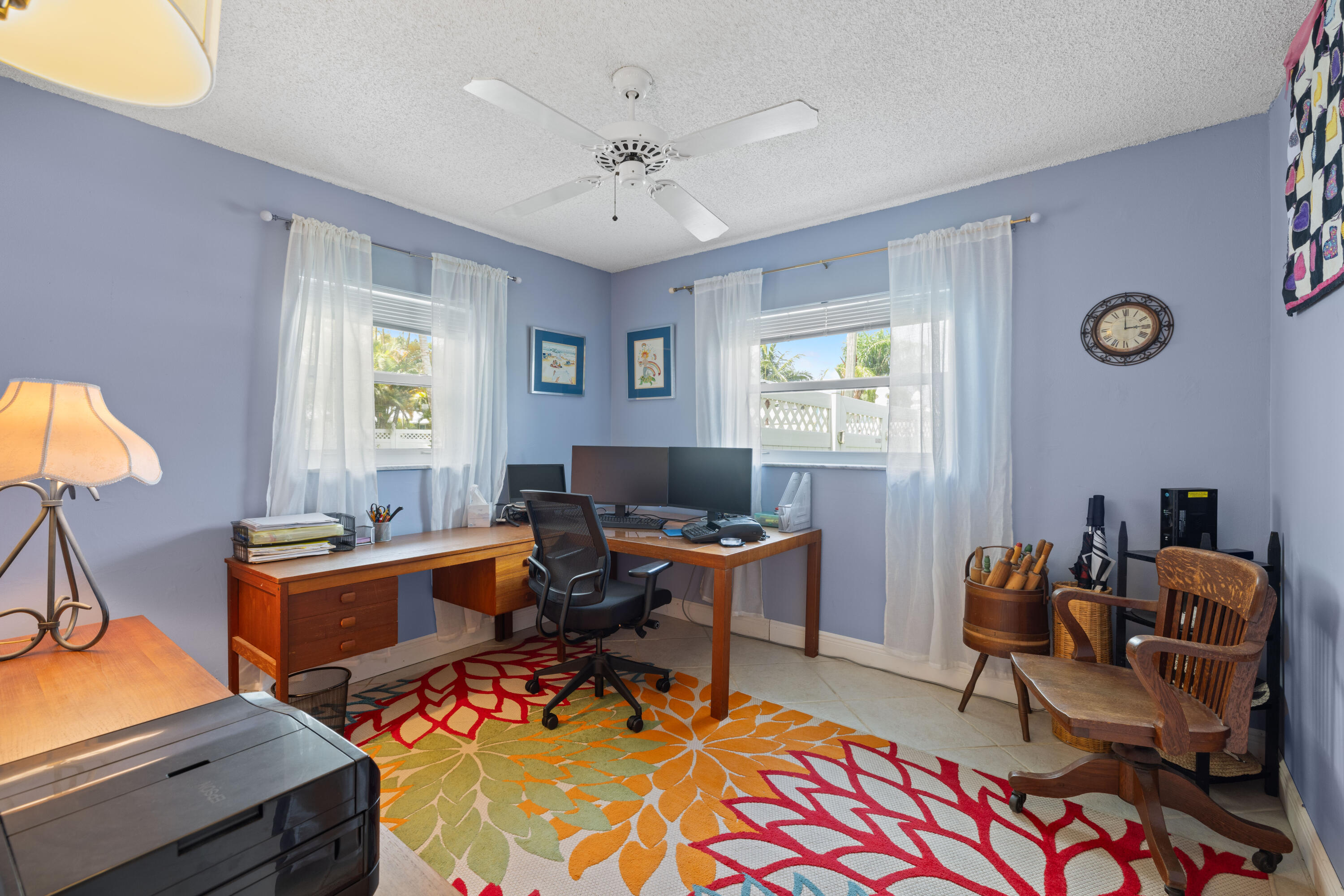 Home office with a wooden corner desk, multiple monitors, and a colorful patterned rug.