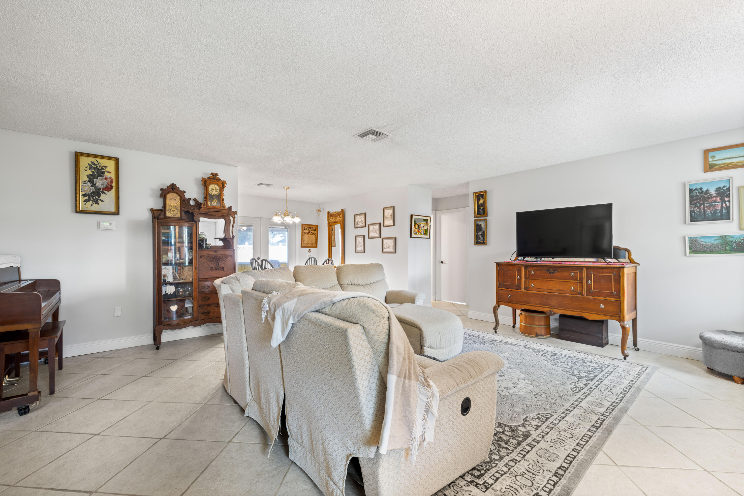Living room with cream sectional, patterned rug, antique cabinets, and television.