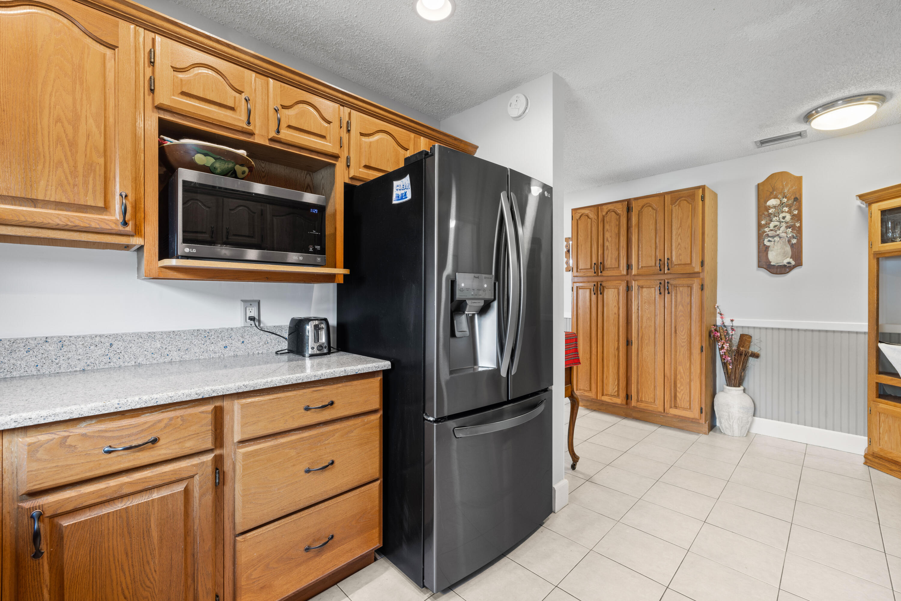 Kitchen with honey-colored wood cabinets, speckled counters, and a black side-by-side refrigerator.